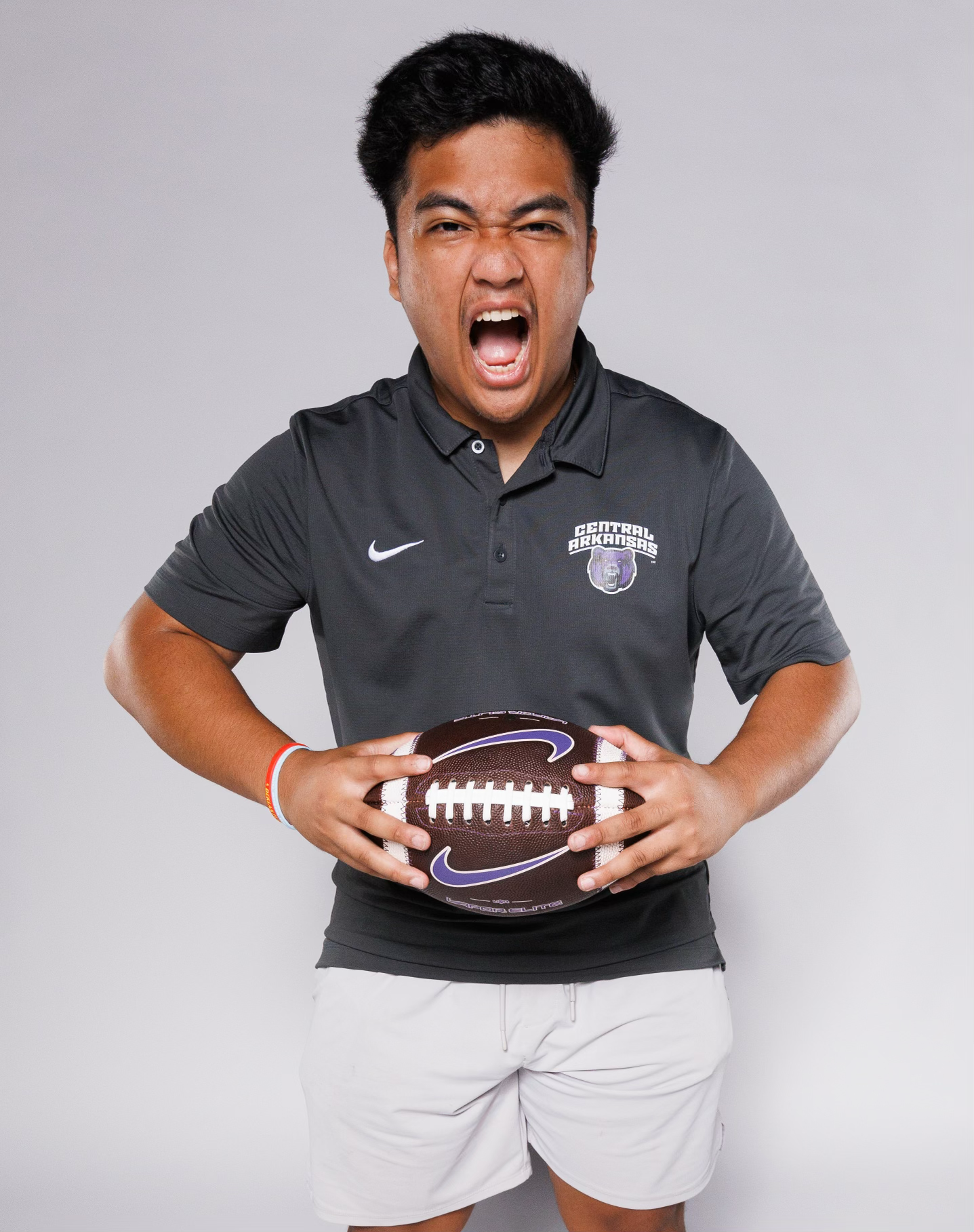 Athletic person in grey Nike polo holding football with energetic expressions.