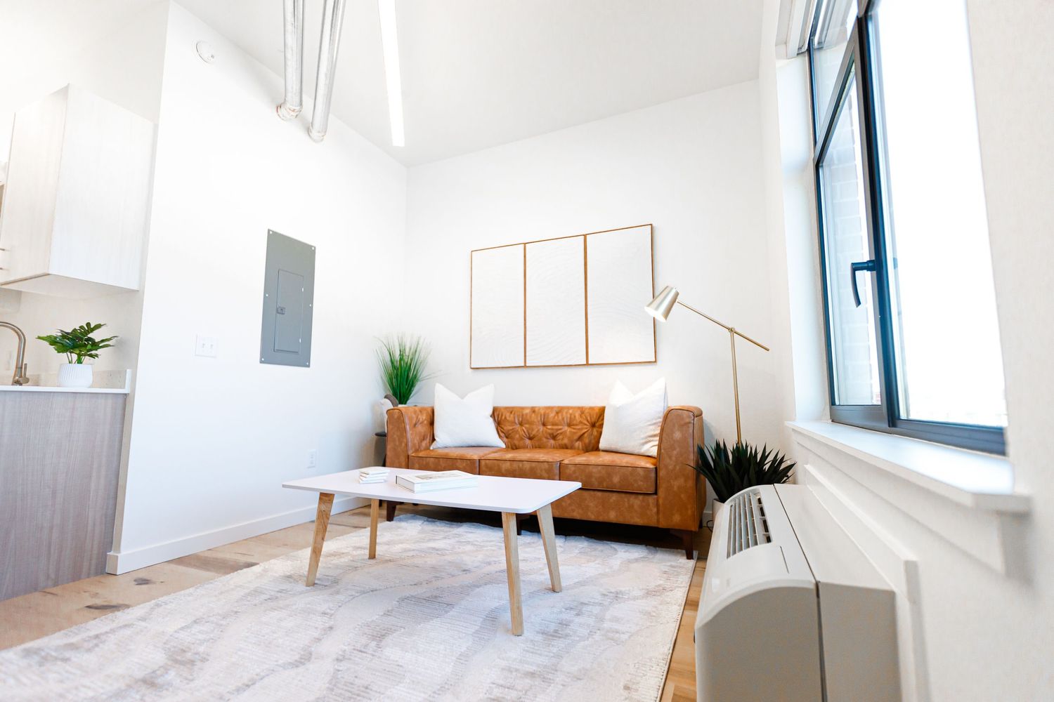 Contemporary living area with camel leather couch, wooden coffee table, and large window.