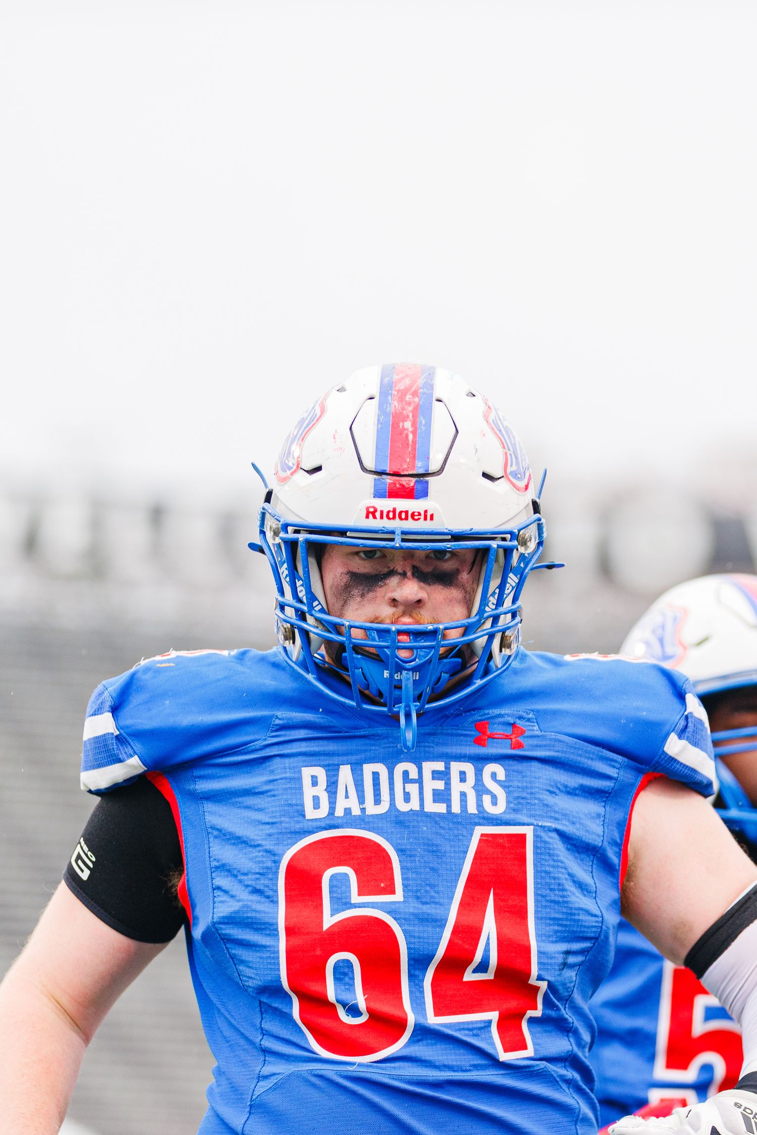 Close-up of Badgers football player number 64 in blue uniform and white helmet.