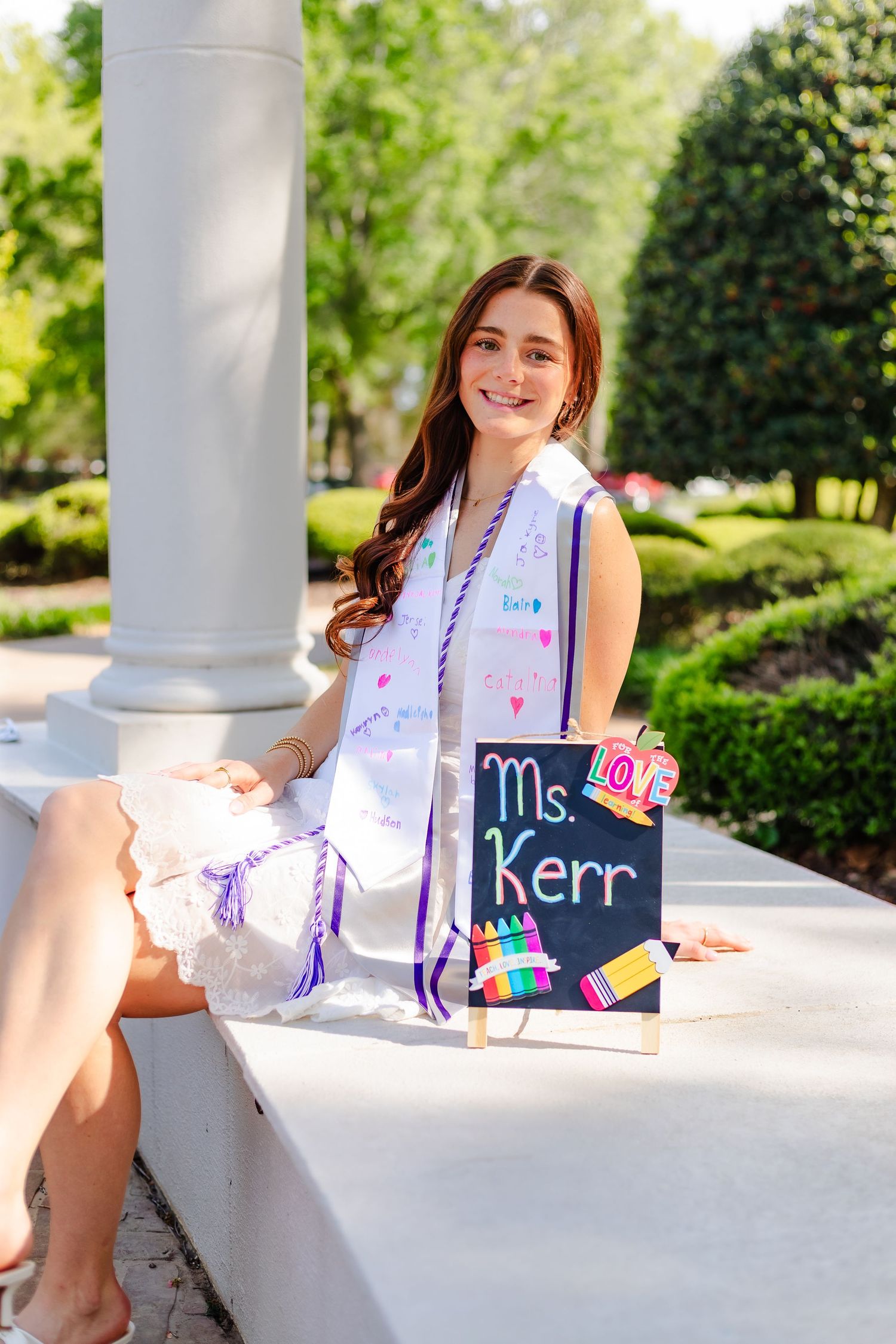 White dress and floral shawl against column backdrop, with chalkboard decorative signs visible.