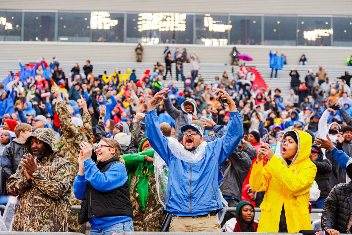 Excited fans in blue and yellow jerseys cheer enthusiastically in the stadium stands during a football game.