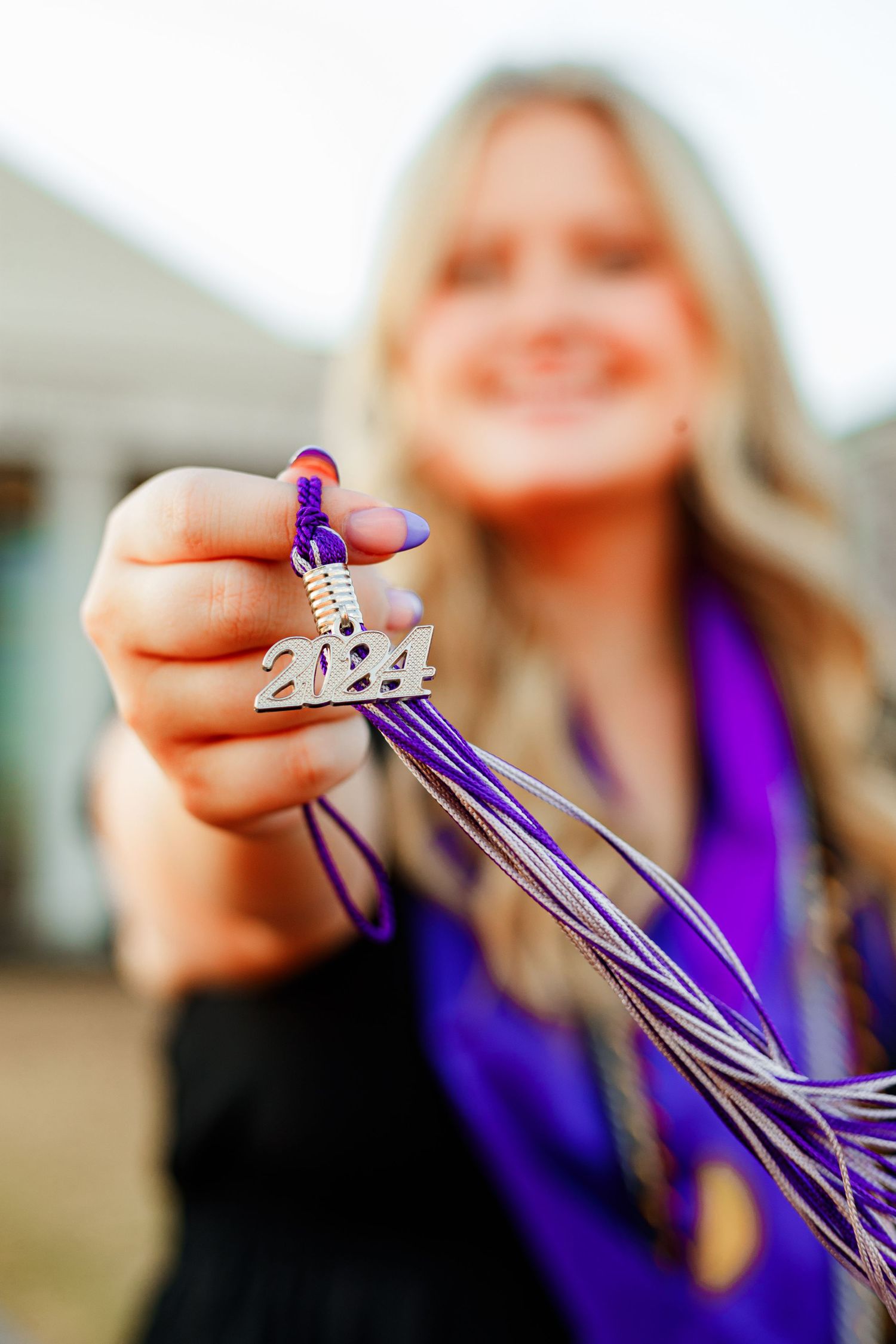 Close-up of purple graduation tassel with 2022 charm held against blurred background.