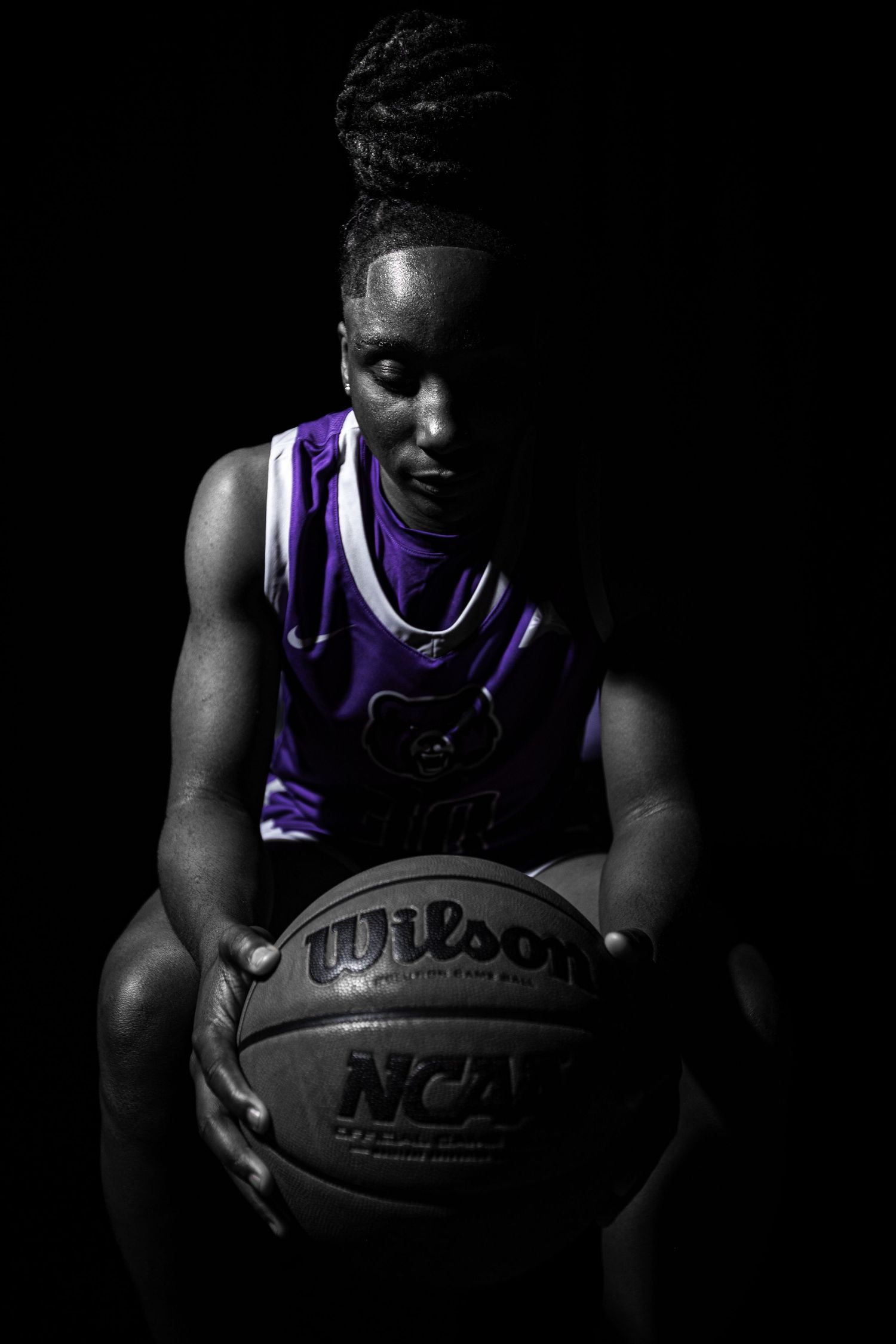 Dramatic basketball portraits in dark lighting with player holding NCAA ball in purple jersey.