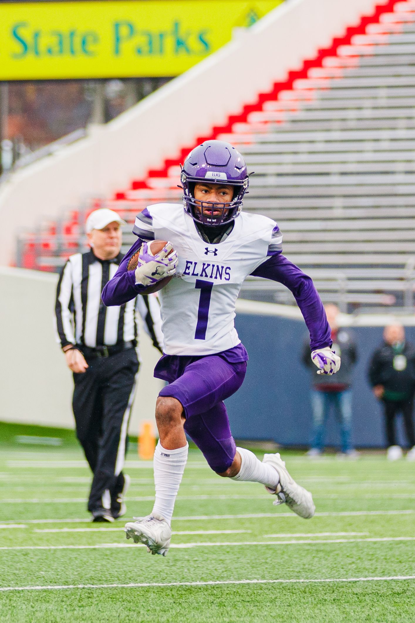Football player in purple and white Elkins uniform runs with ball during game.