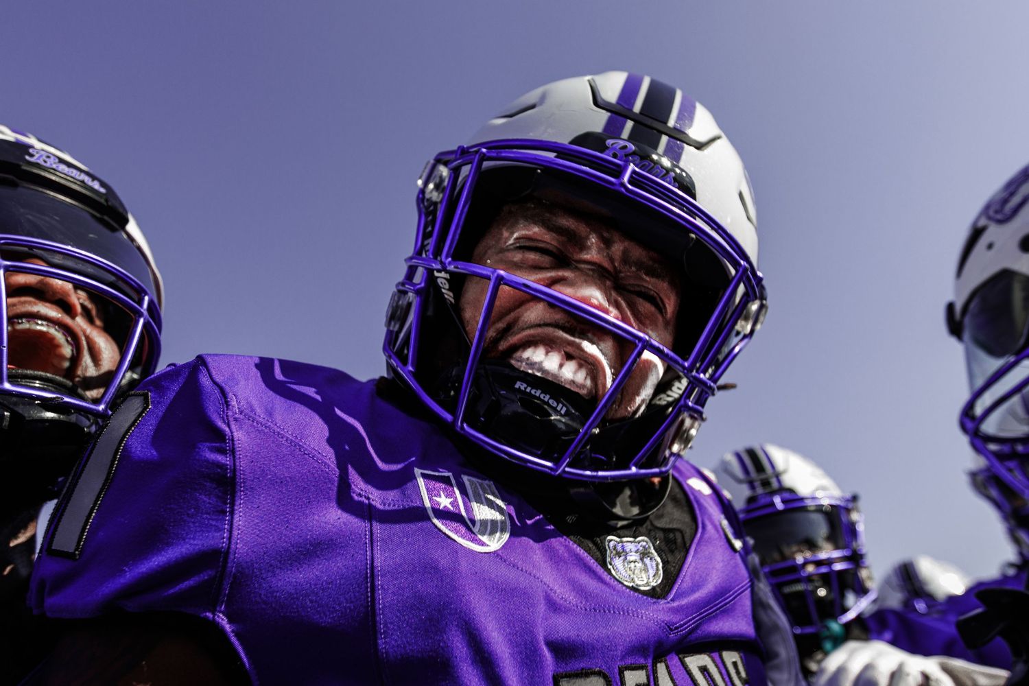 Football player in purple uniform celebrates enthusiastically under bright blue sky.