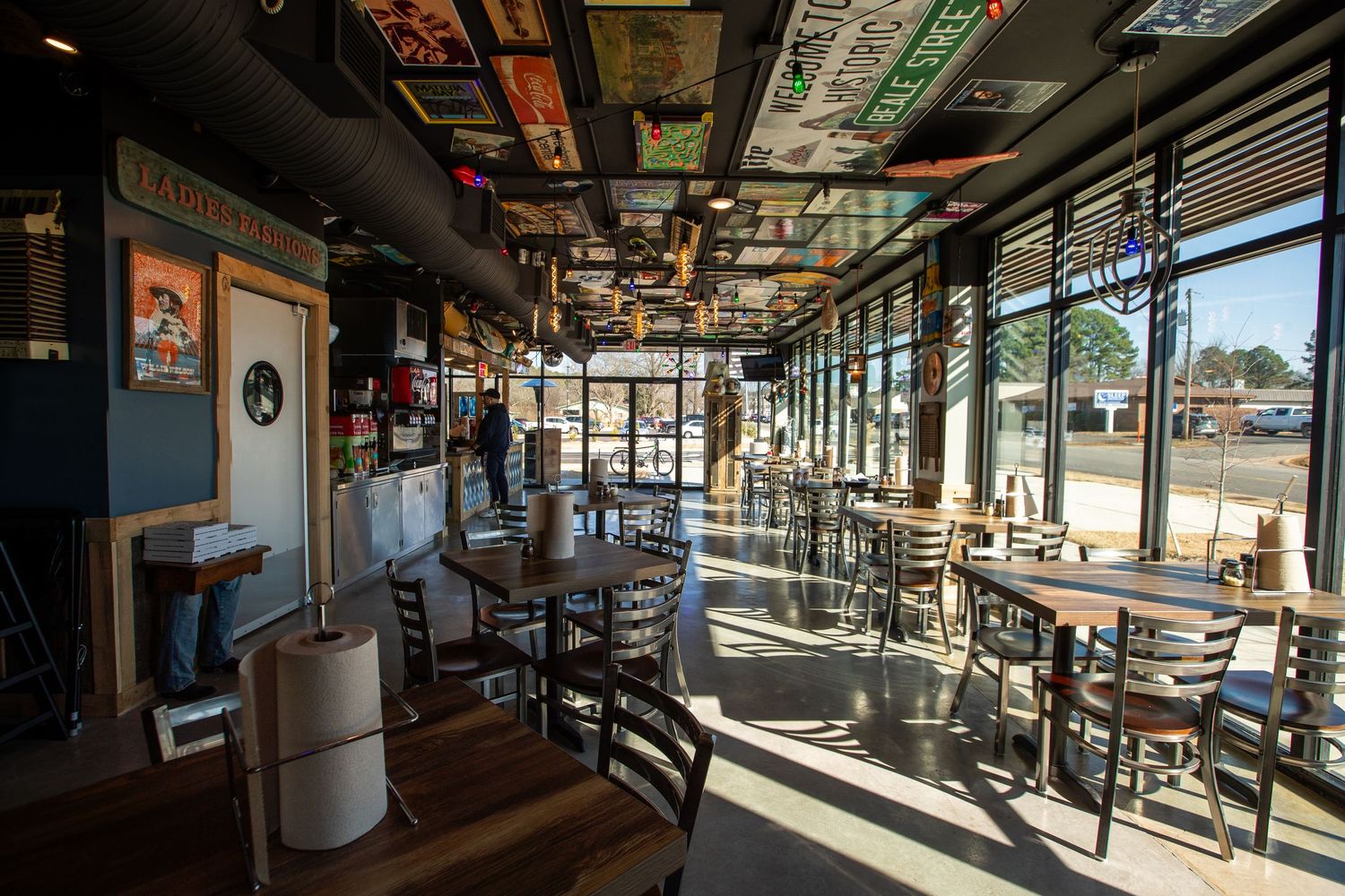 Sunlit restaurant dining area with wooden tables and chairs lined along windows.
