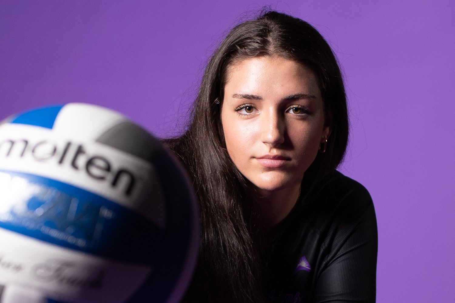 Dramatic portraits of athletes with volleyball against purple background.
