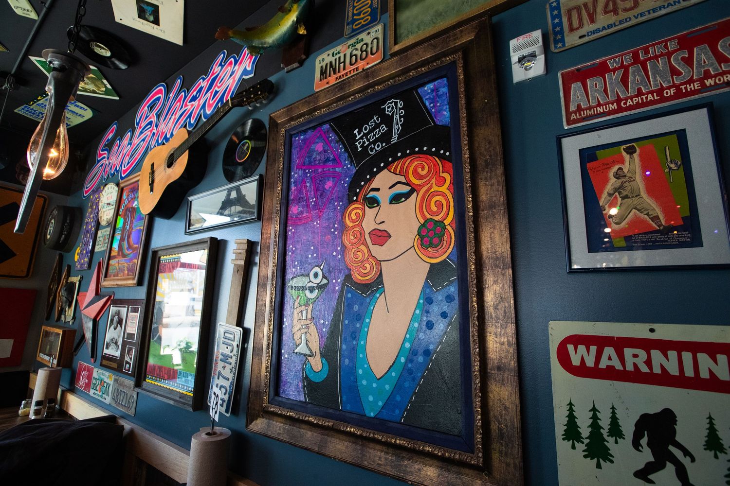 Colorful wall art featuring neon signs and pop art style portrait in bar setting.