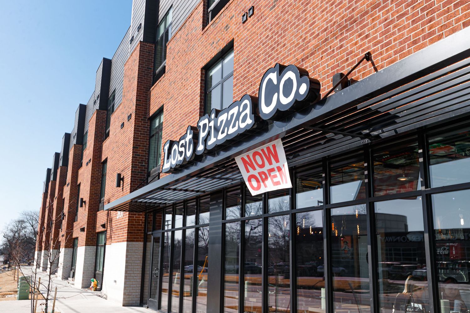 Lost Pizza Co. restaurant exterior with red brick facade and 'Now Open' sign.
