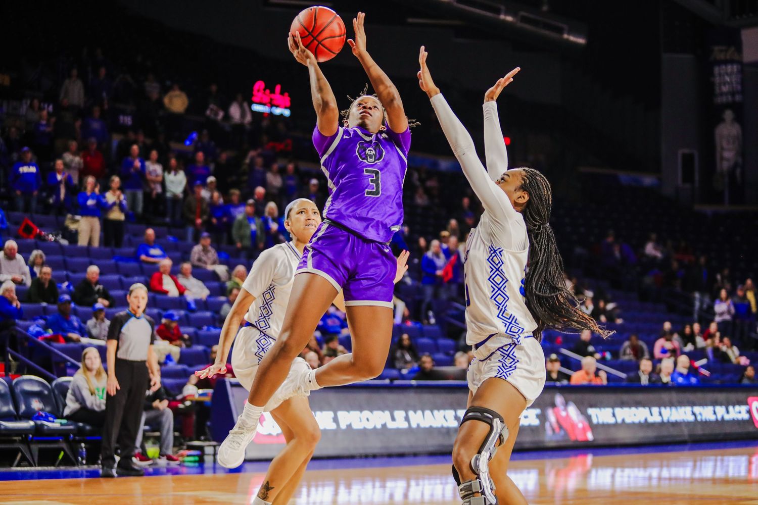 Basketball player in purple jersey takes jump shot during competitive game.