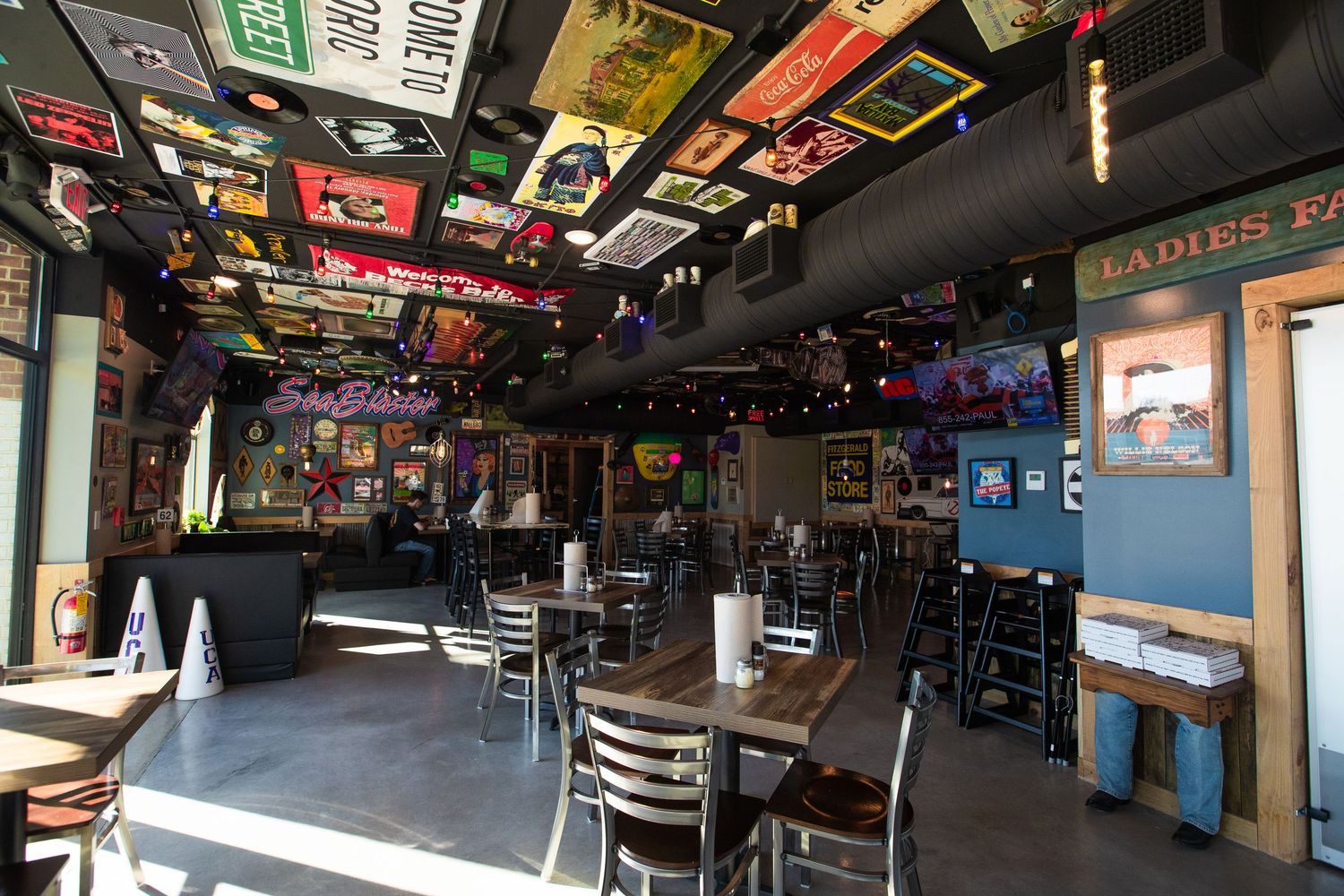 Restaurant interior with tables and chairs under ceiling covered in vintage signs and decorations.
