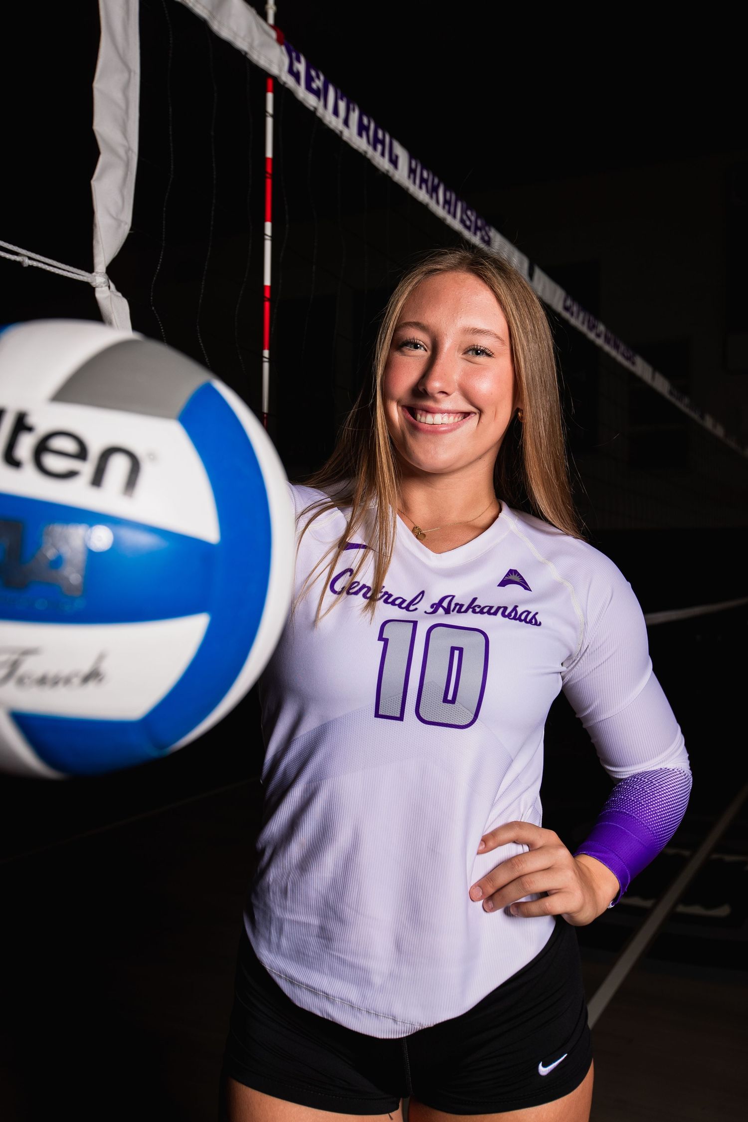 Volleyball player in white uniform poses with ball for sports photography series.