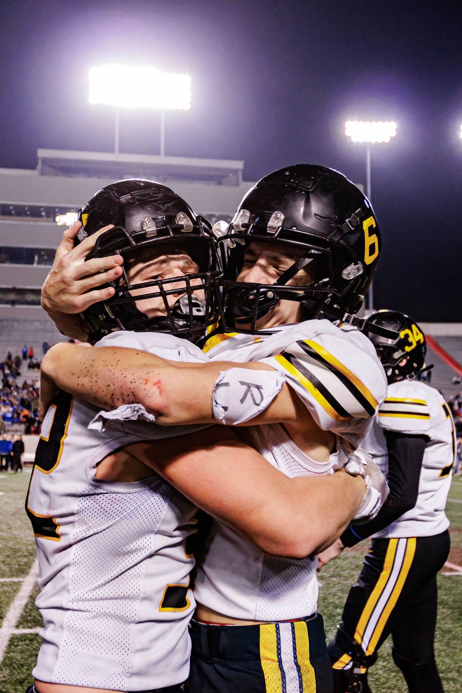 Football players in white and black uniforms embrace in celebration under stadium lights.