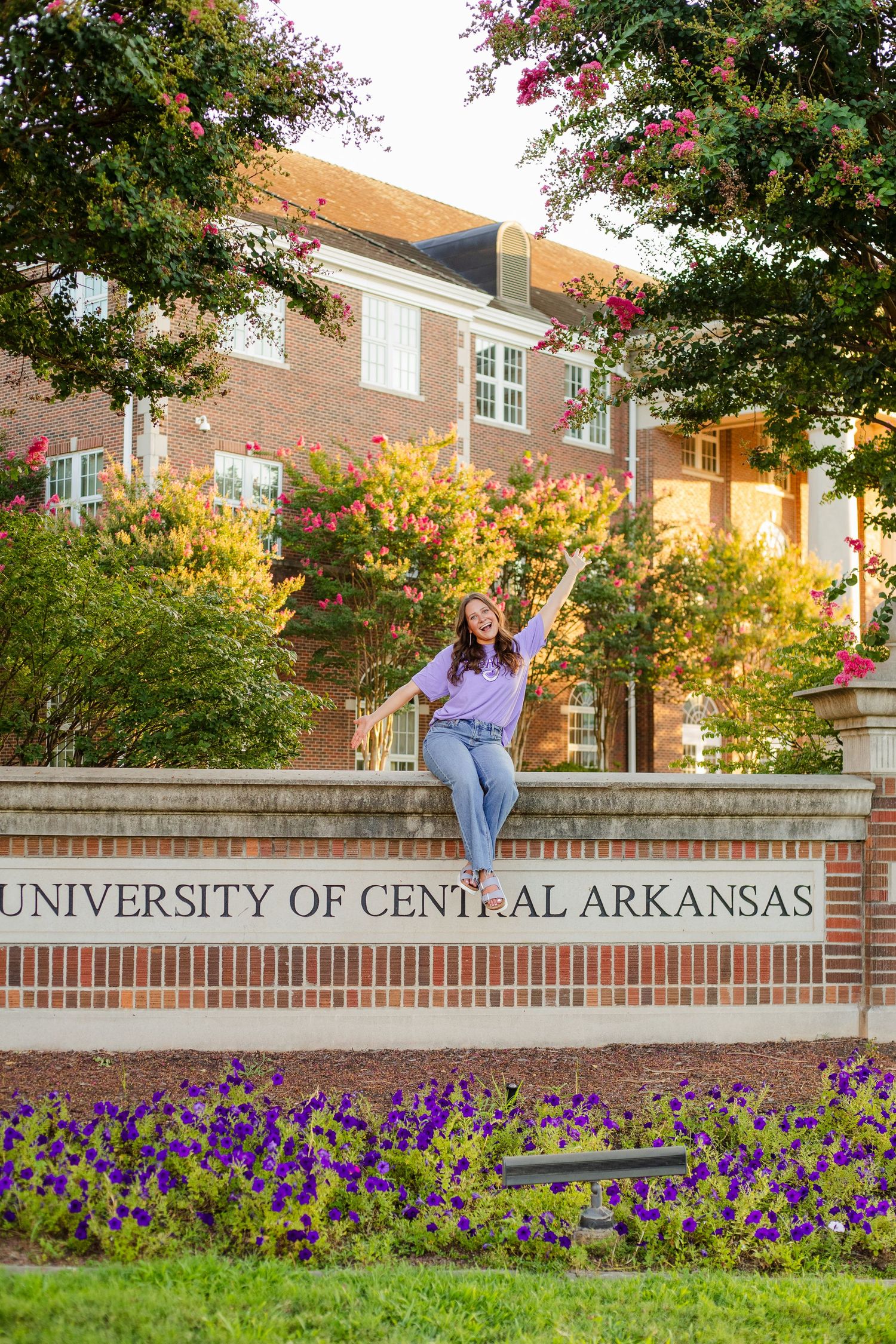 Purple flowers bloom beneath the University of Central Arkansas entrance sign on a sunny autumn day.