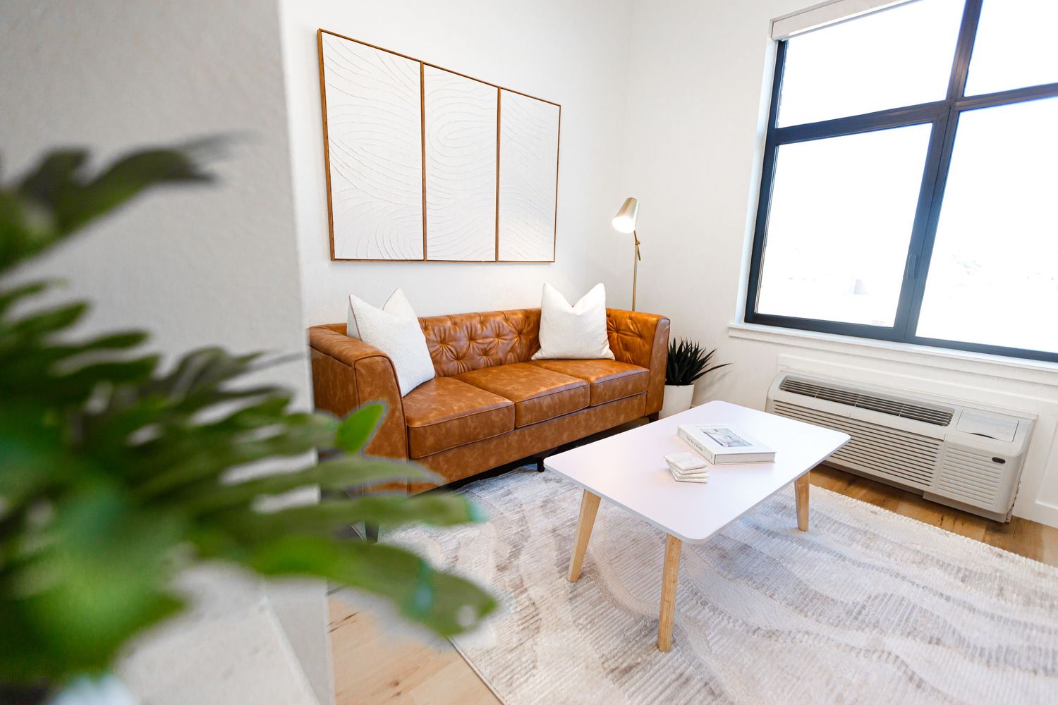Contemporary living room with brown leather couch, marble coffee table, and potted plants.