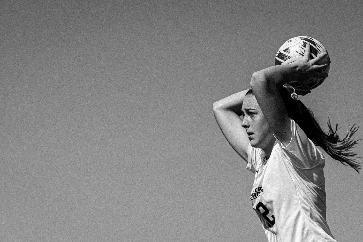 Soccer player in white uniform throws ball in during black and white action shot.