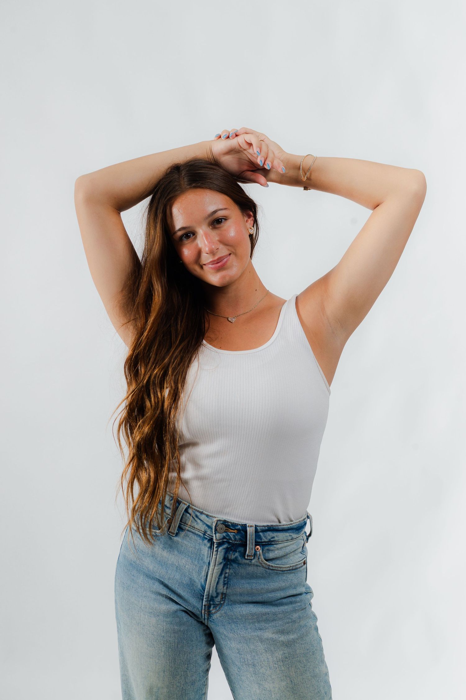 A person in a white sleeveless top and light wash jeans strikes playful poses against a white background.