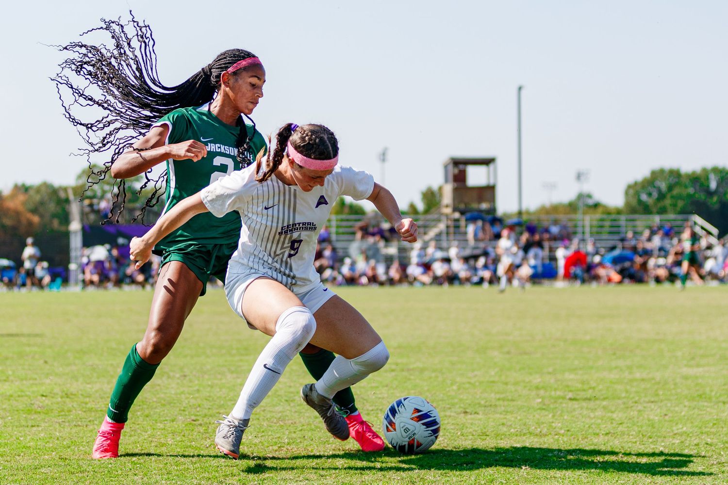 Soccer players competing for ball during match on sunny grass field.