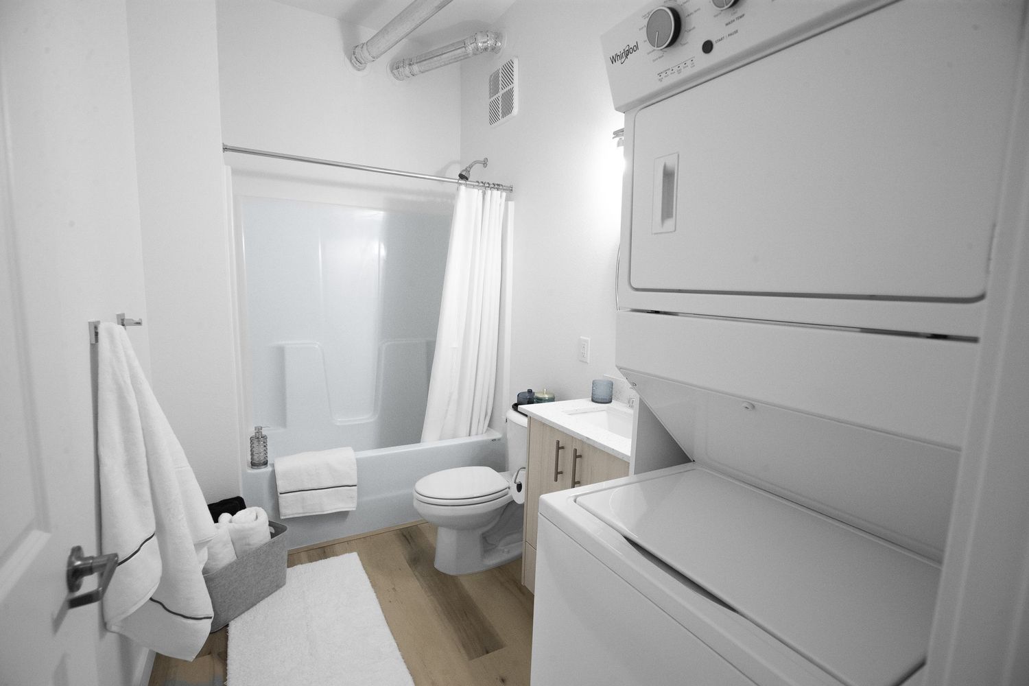 Modern white bathroom featuring stacked washer and dryer, shower curtain, and clean minimalist design.