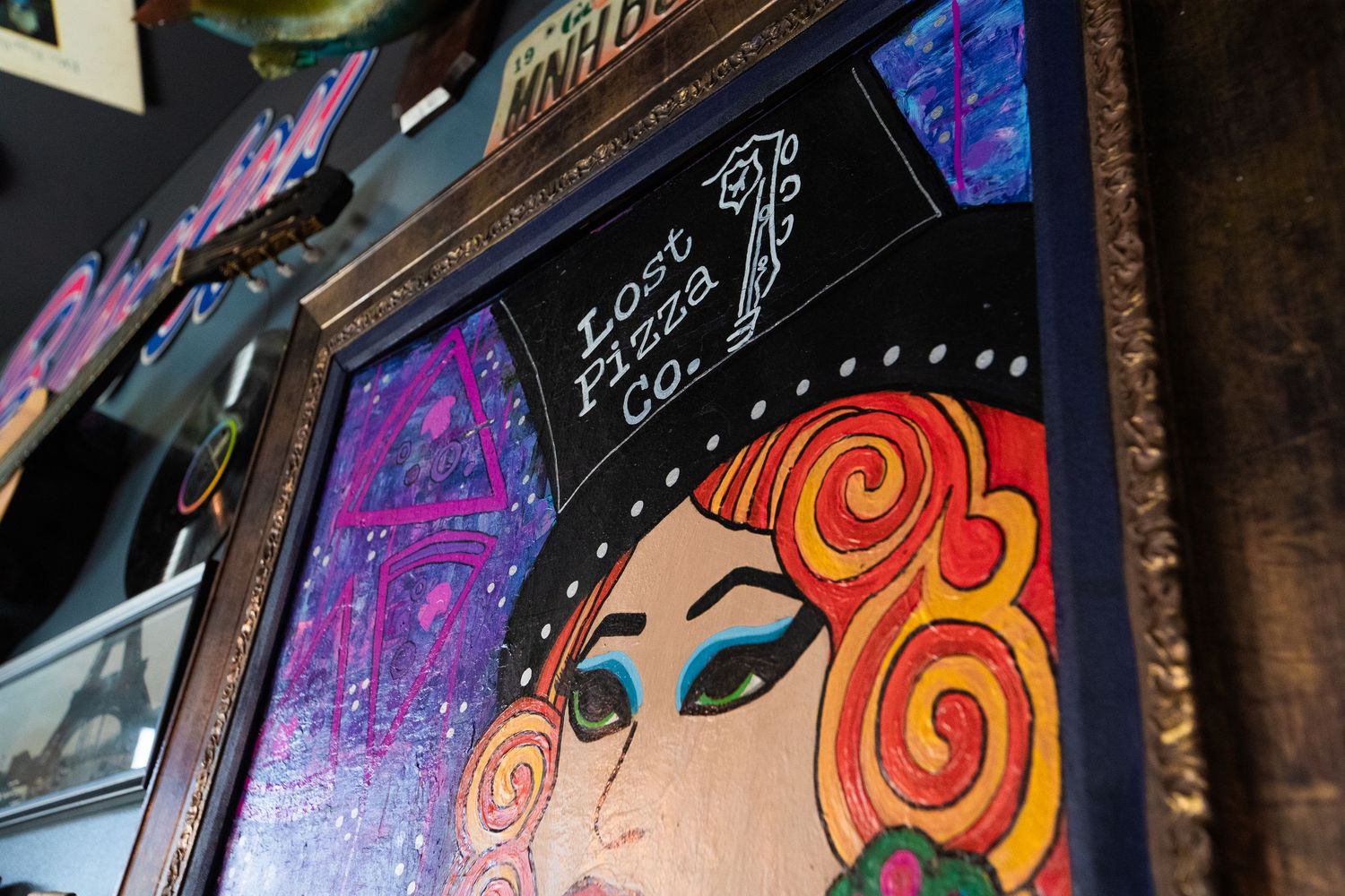Close-up of framed artwork featuring stylized portrait with orange swirled hair against purple background.