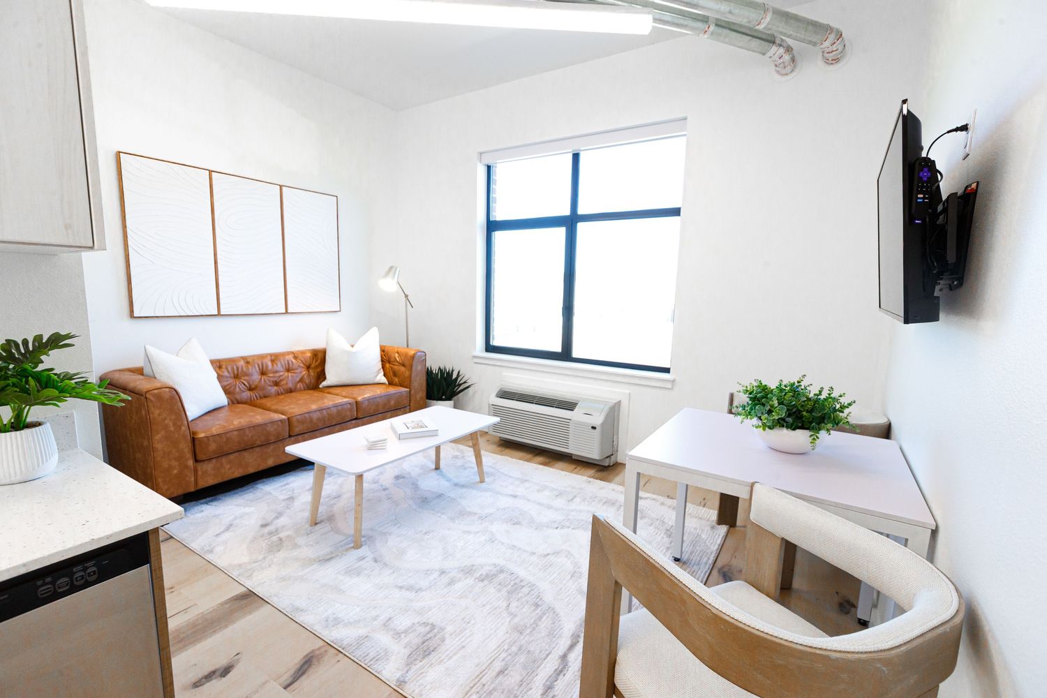 Bright studio apartment with leather sofa, marble coffee table, and blue-framed window.