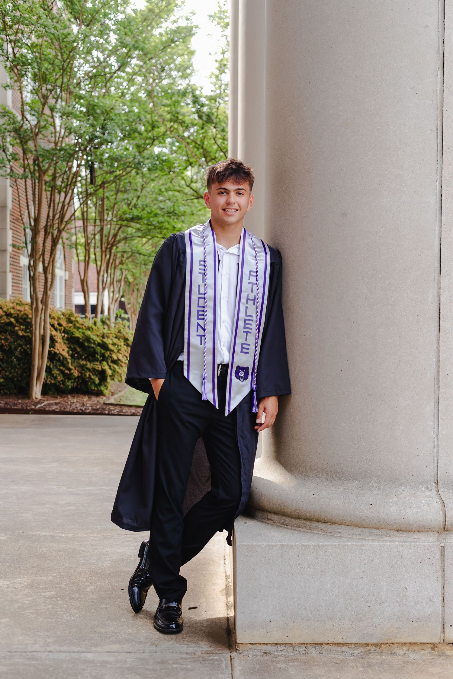 Graduate in cap and gown poses for a series of graduation photos in front of white columns on campus.