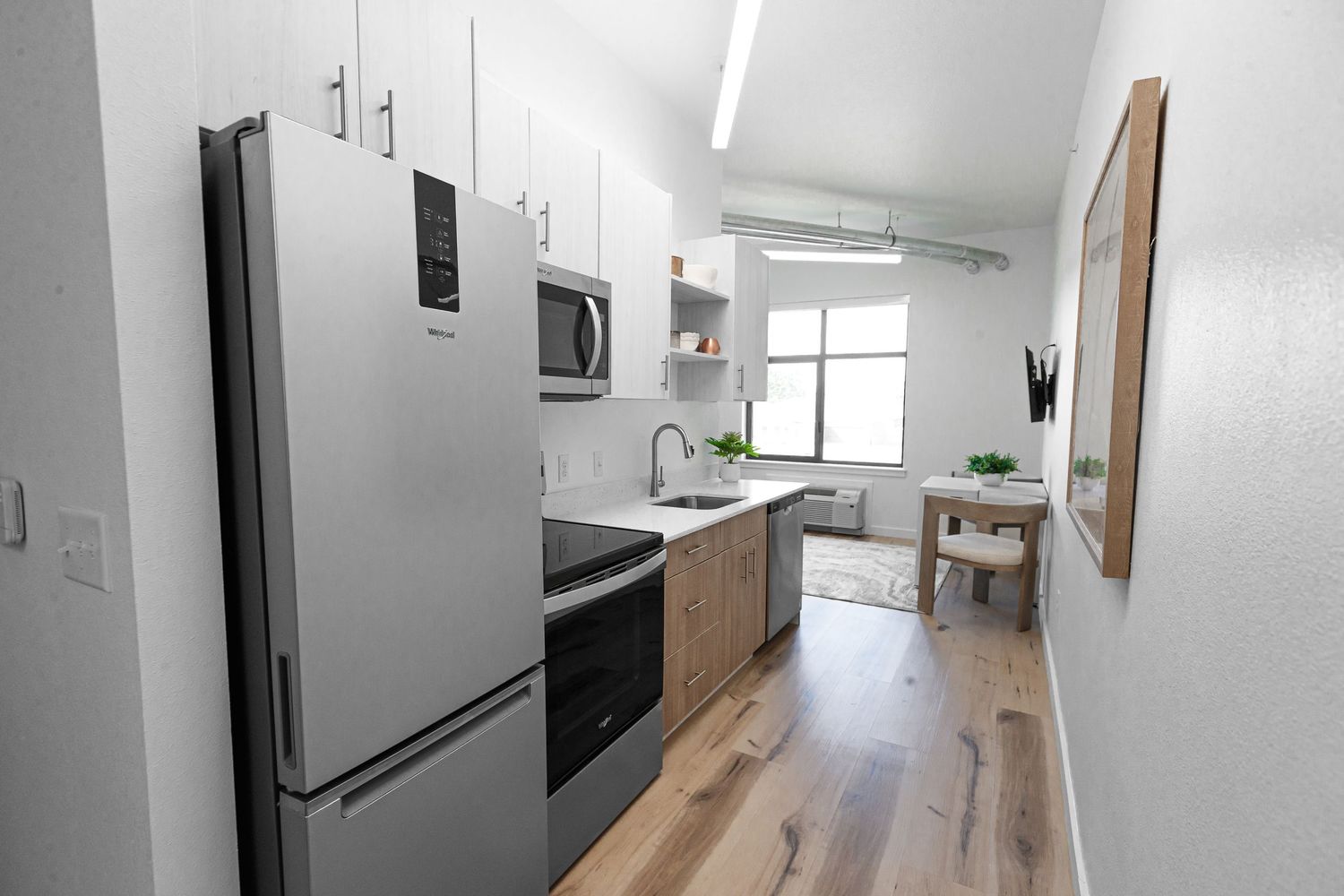 Modern galley kitchen with stainless steel appliances and hardwood flooring in bright white space.