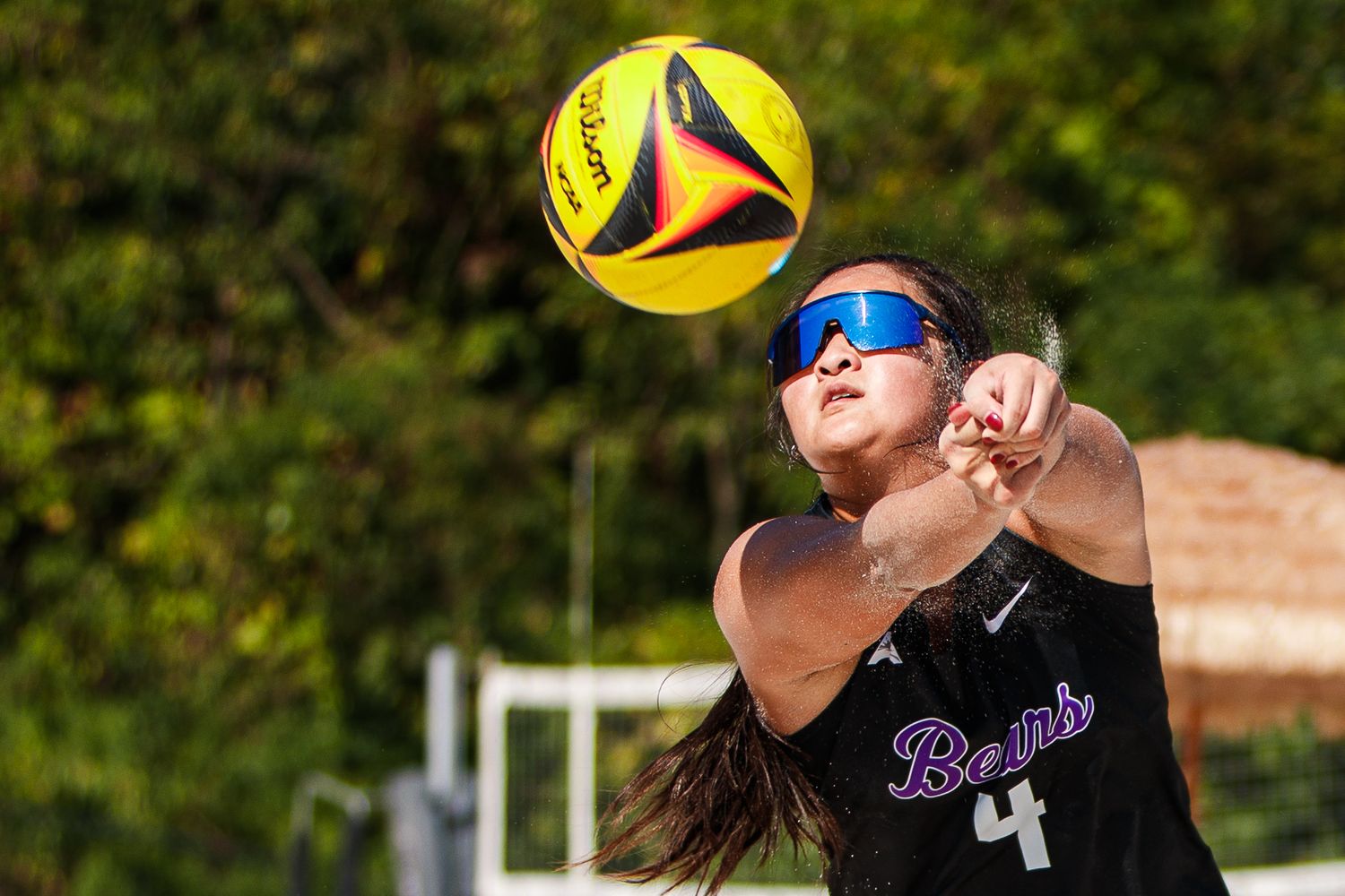 Beach volleyball players leap to hit yellow balls during an outdoor match.