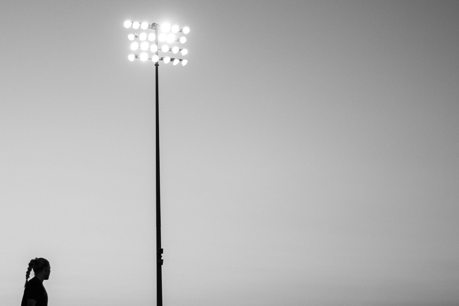 Stadium floodlights illuminate a sports field against a gray evening sky.