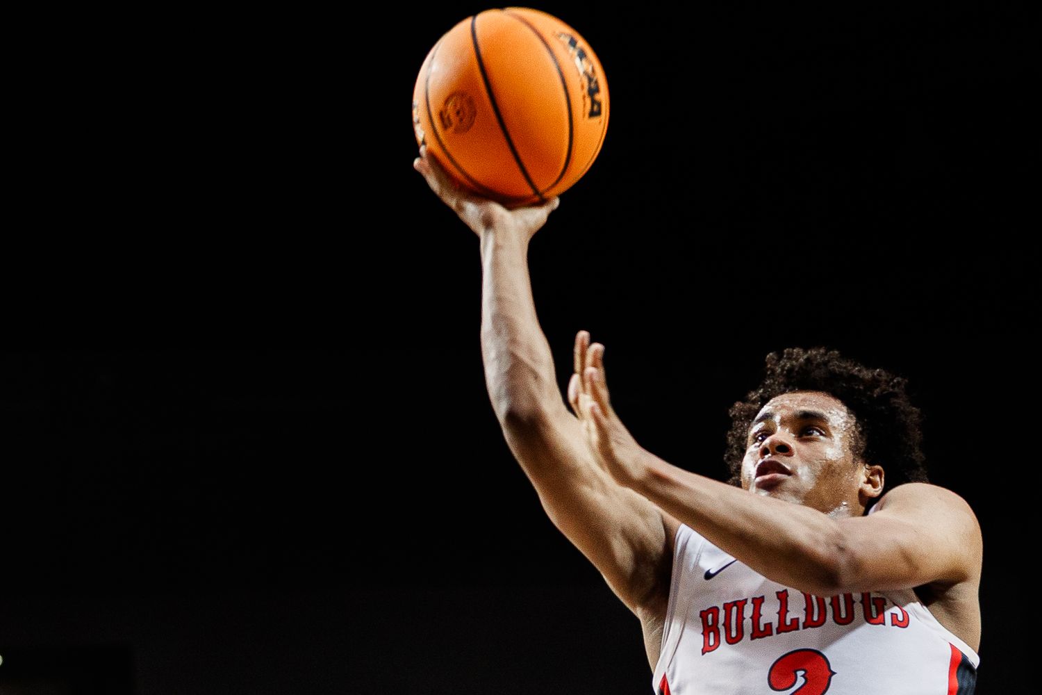 Basketball in mid-air during game with players reaching for rebound.