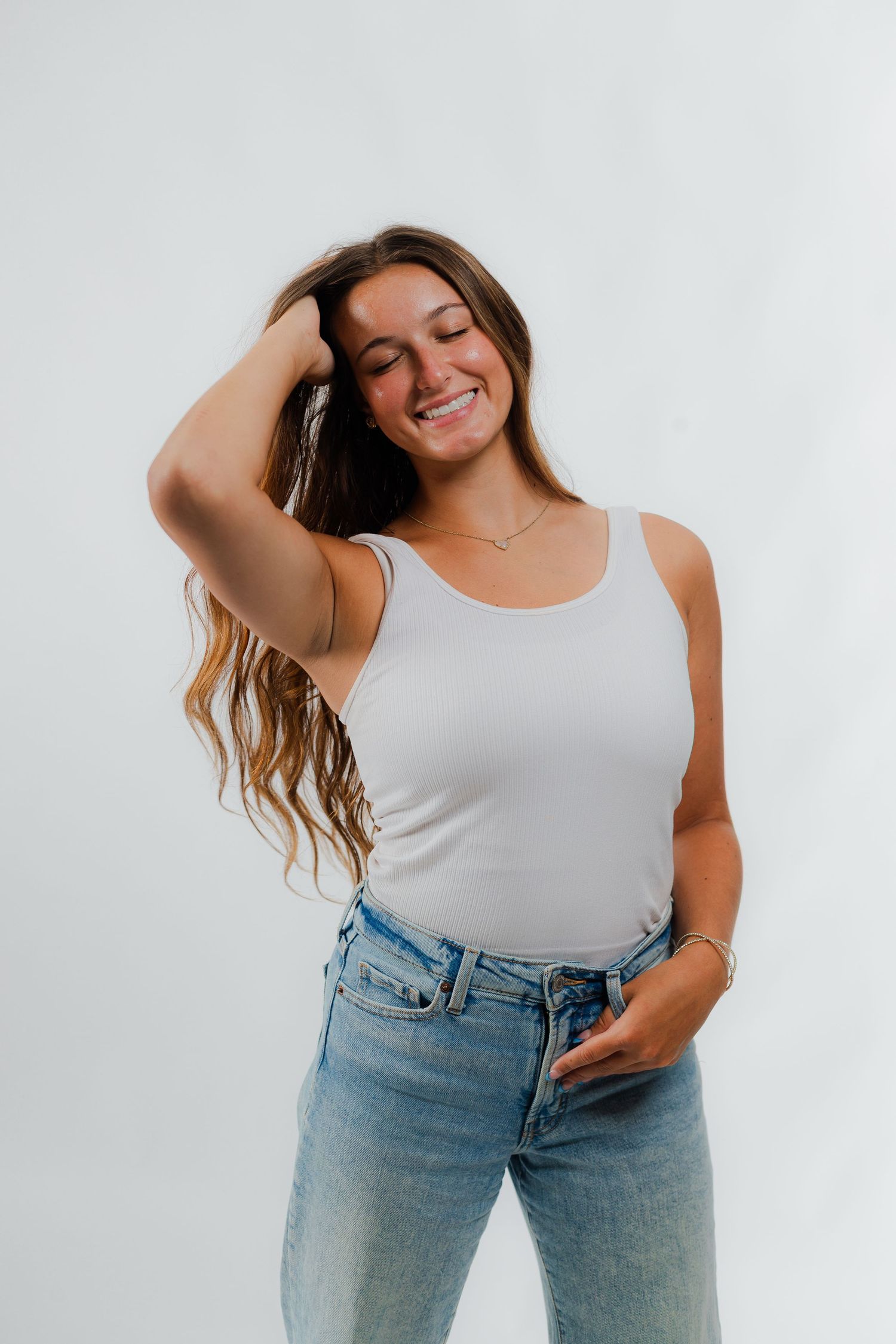 Casual lifestyle portrait against white background showing person in white tank top and light wash denim jeans.