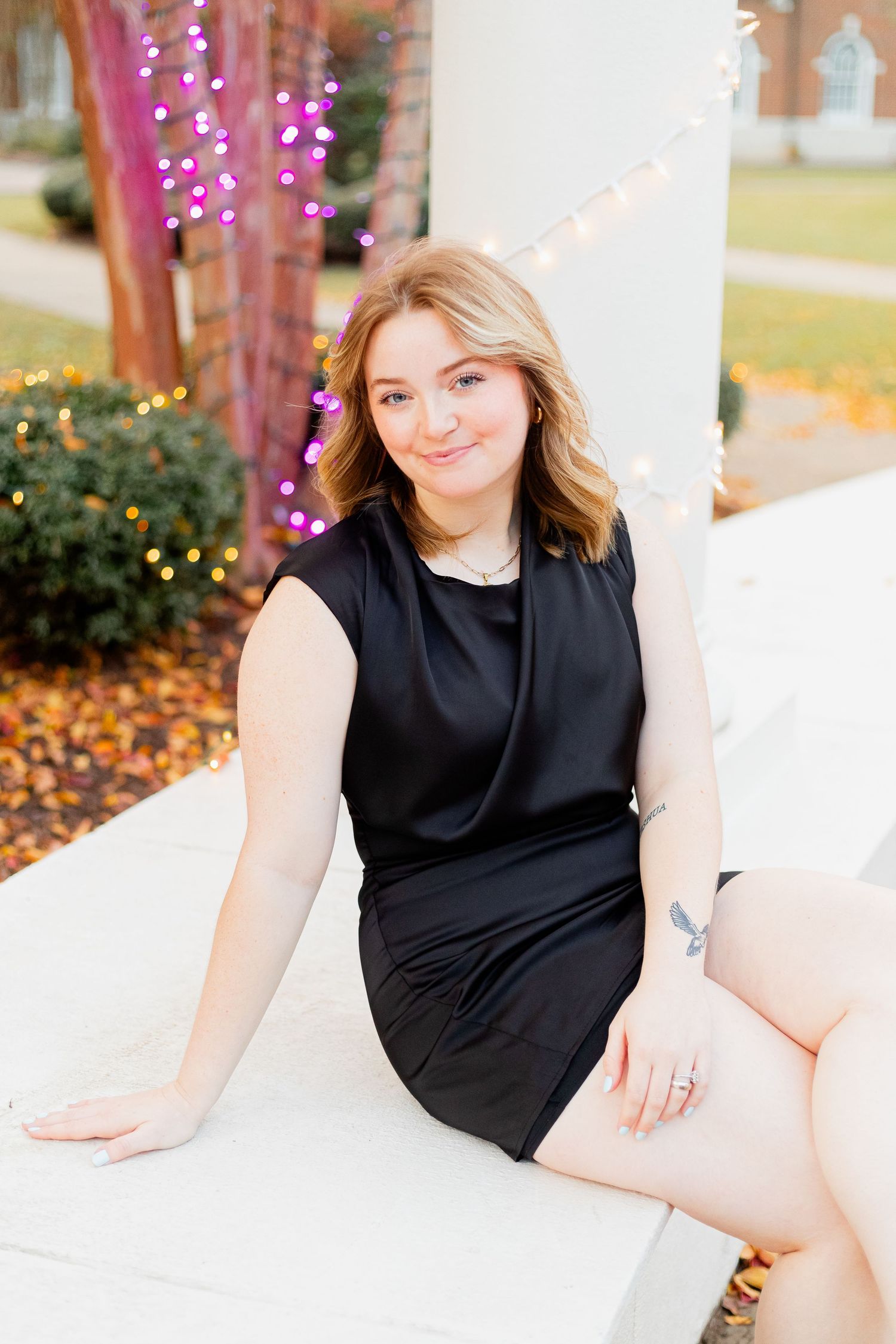 A portrait taken outdoors with decorative lights and autumn foliage in the background.