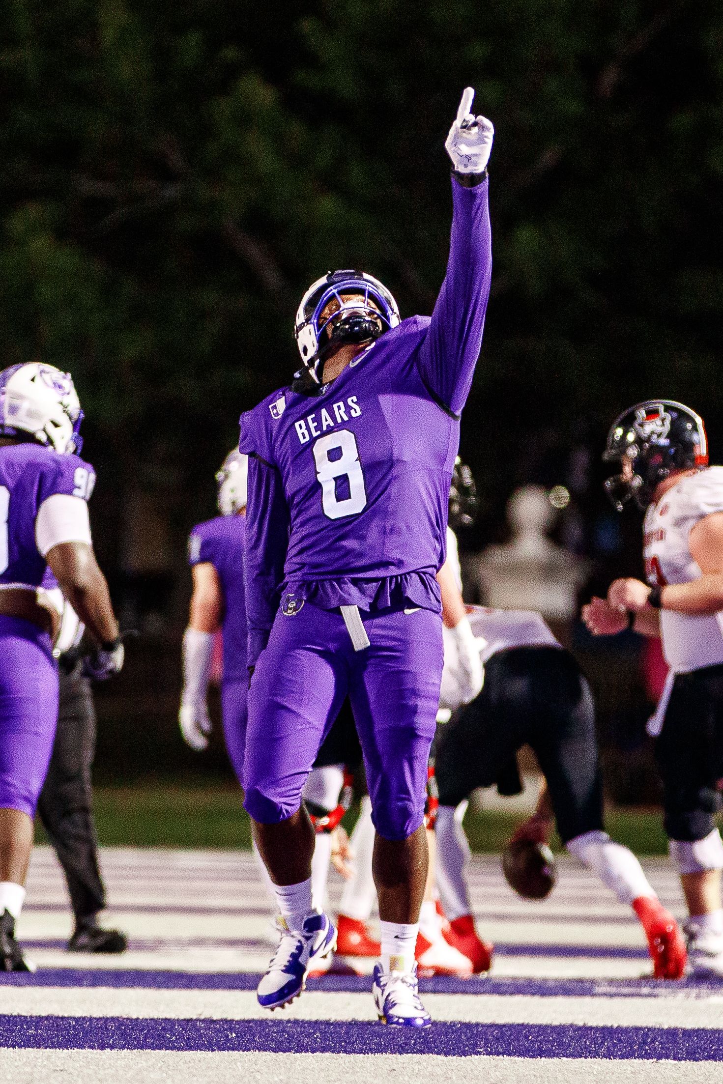 Football player in purple Bears jersey celebrates with raised hand gesture in sports arena.
