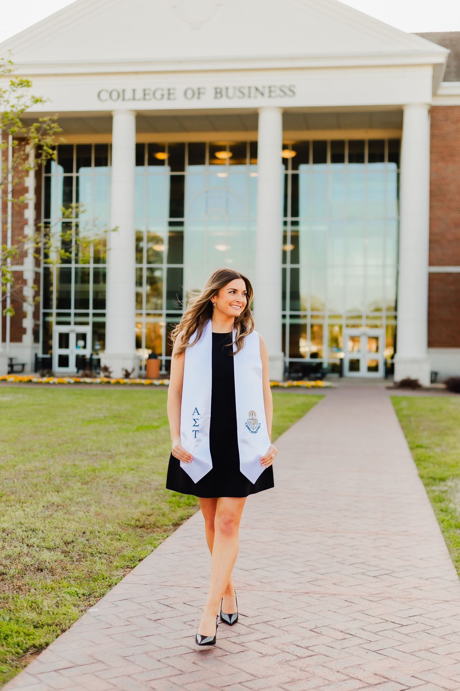 A graduate takes photos in front of the College of Business building on a sunny day.