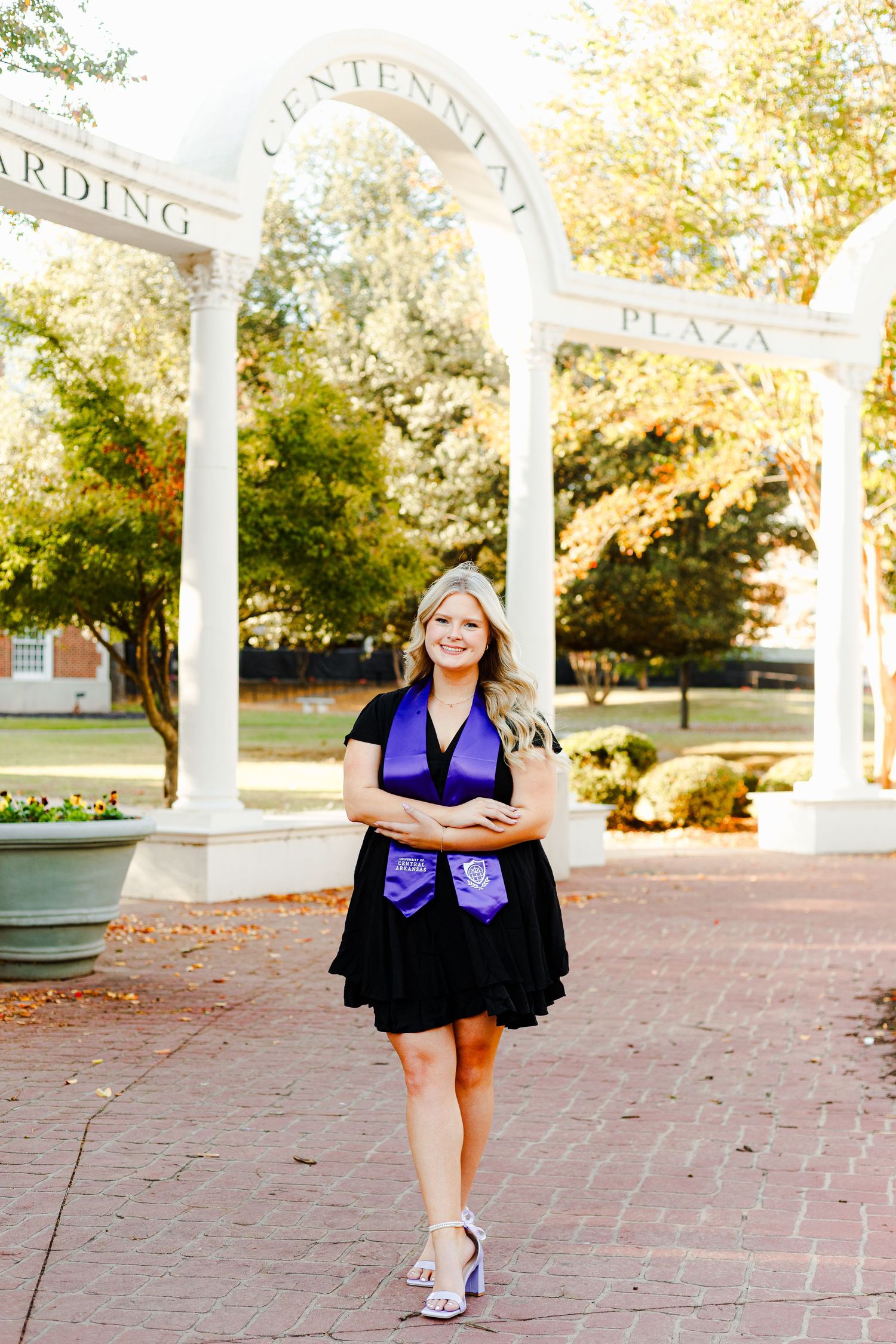 Graduate in purple stole walks confidently between white columns during photo shoot.