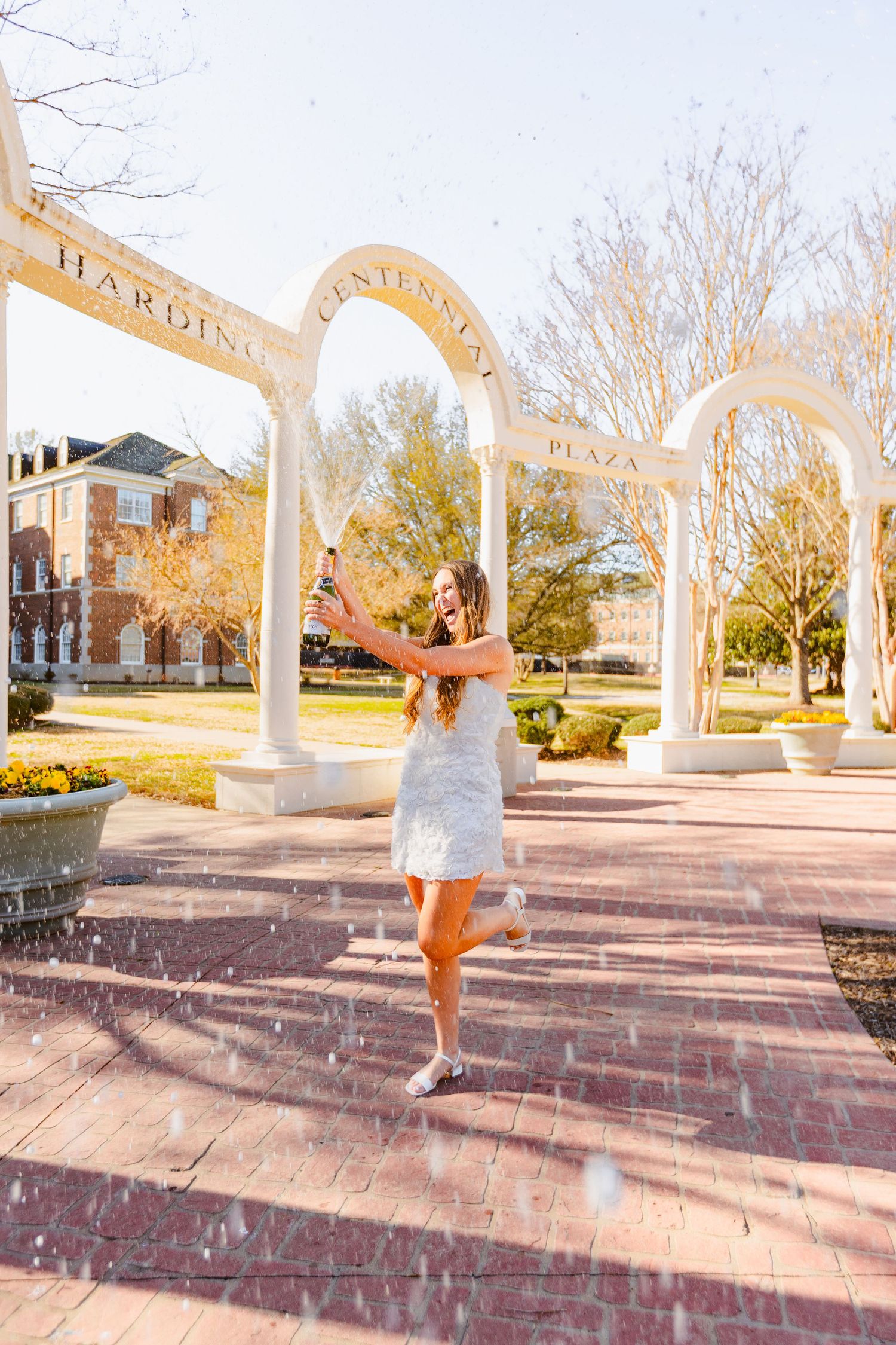 A person in a white dress twirling joyfully on a brick pavilion during sunset.