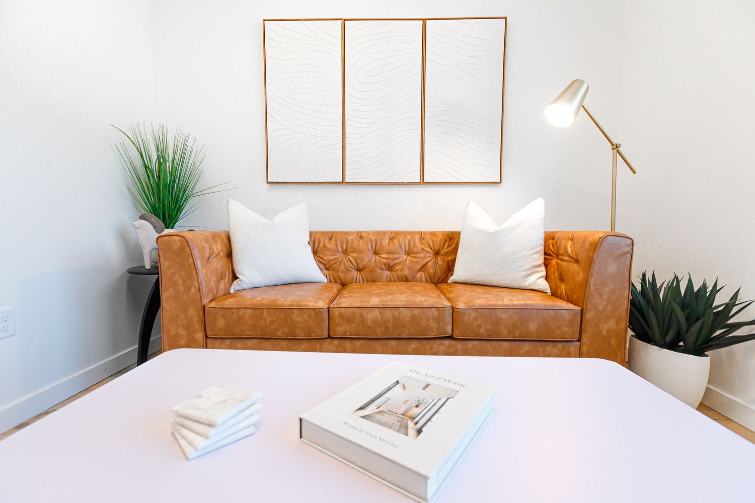Minimalist living area with tan leather sofa, empty wooden frames, and decorative plants.