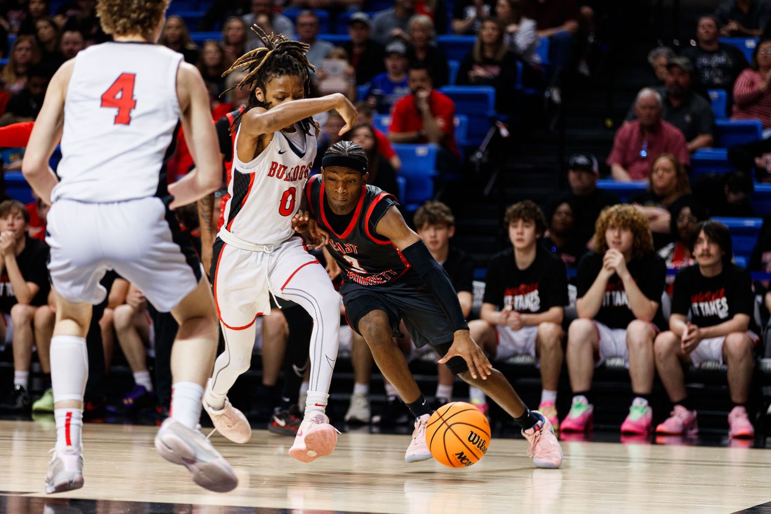 Basketball players compete for possession during an intense game on a brightly lit indoor court.