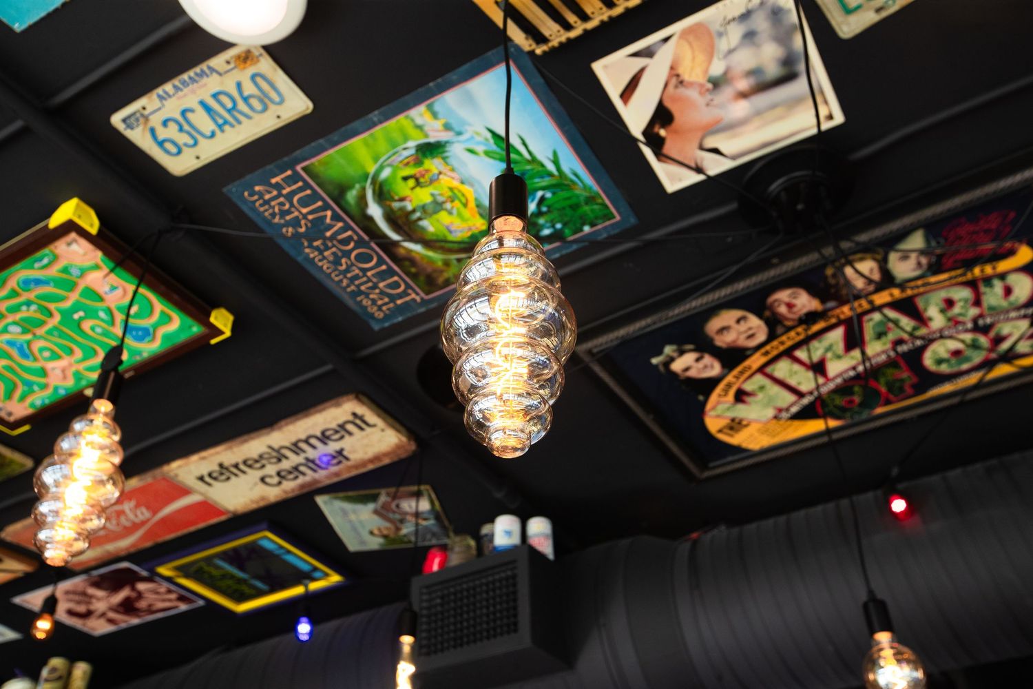 Decorative hanging light fixtures illuminate a ceiling covered with colorful retro signs and memorabilia.