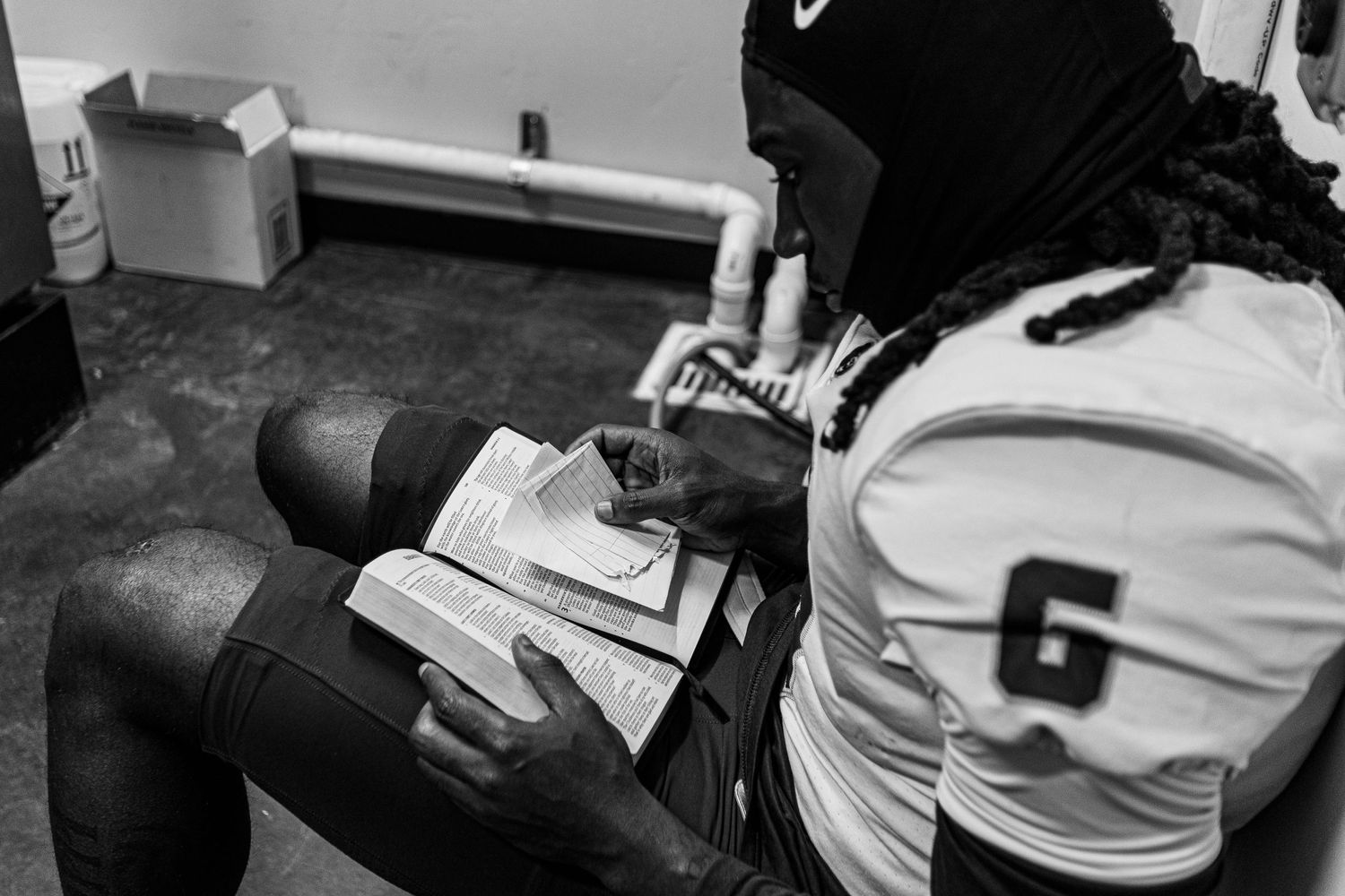 Black and white image of an athlete reviewing notes or playbook in a locker room.