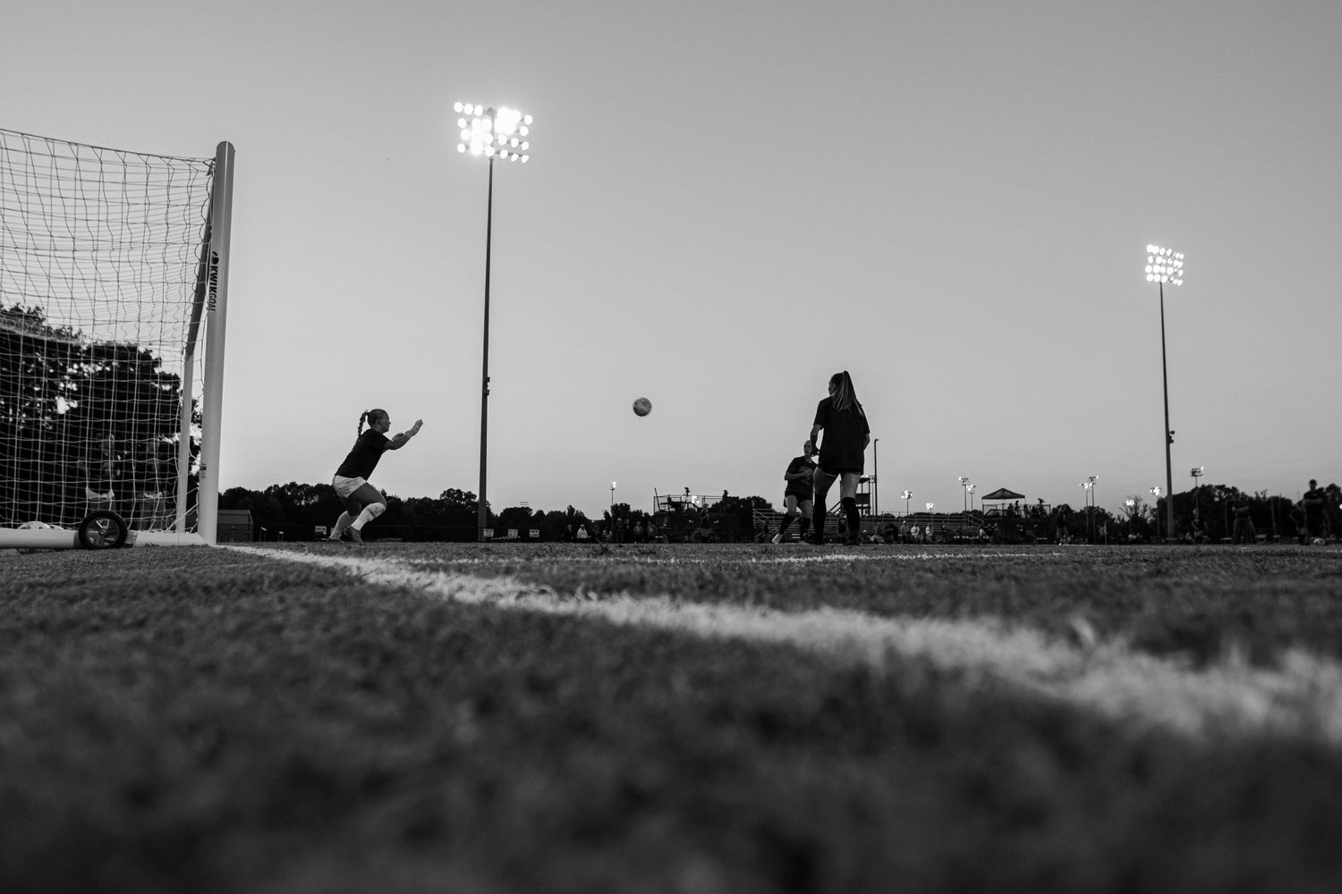 Silhouette of soccer goalkeeper diving to make a save against stadium lights.