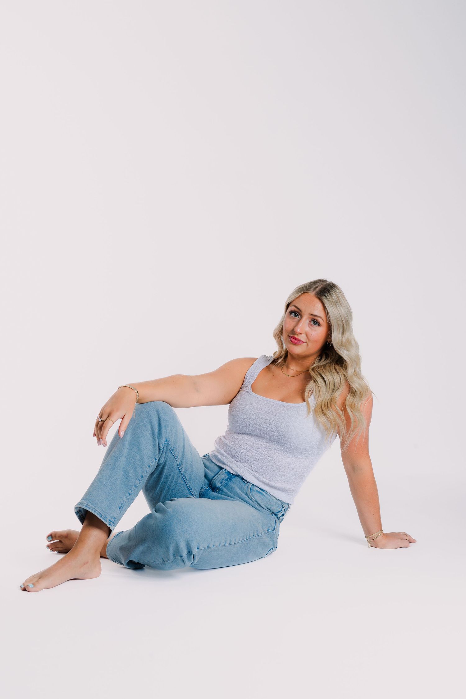 A person in light blue denim jeans and a grey tank top poses on a white background in different casual positions.