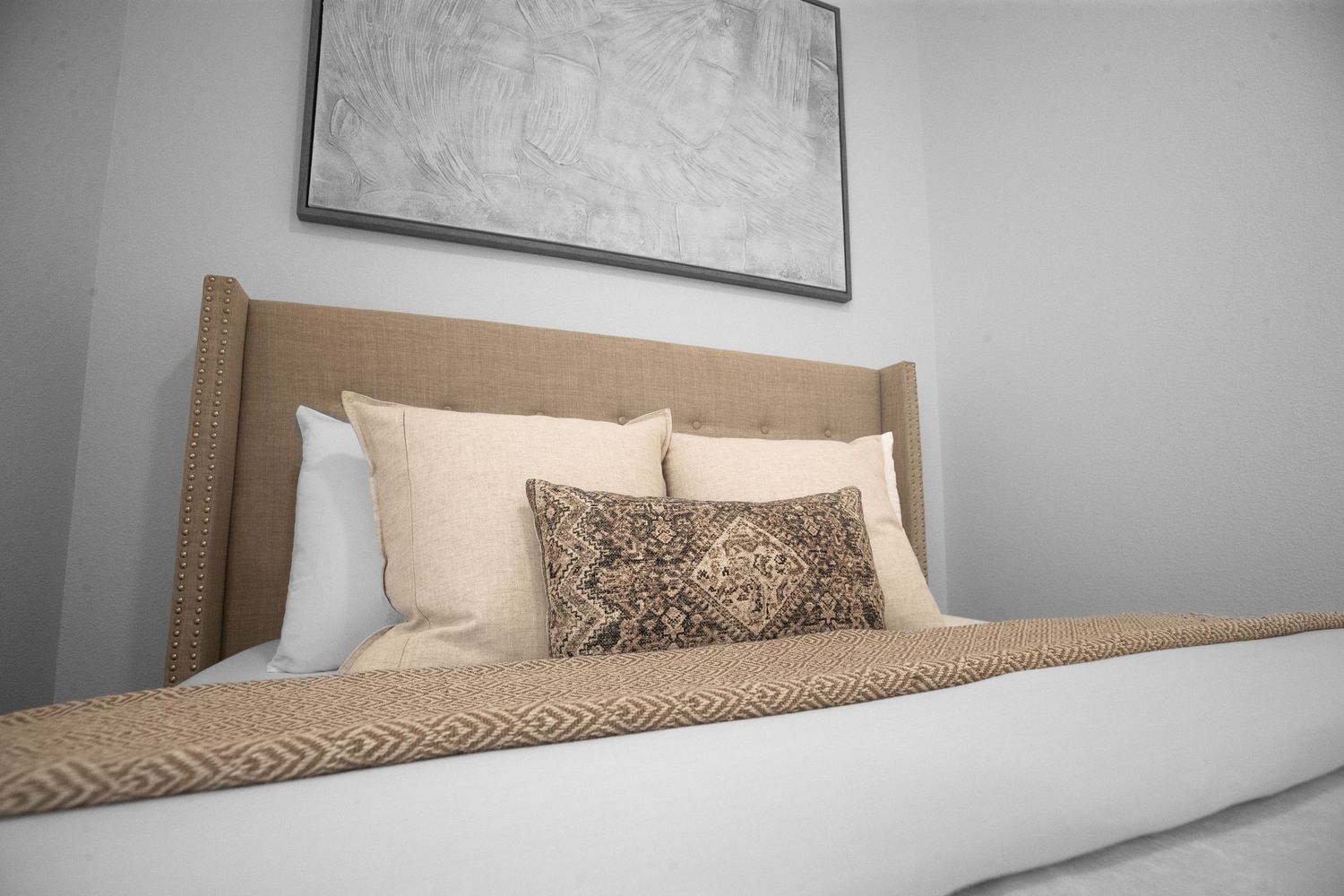 Contemporary bedroom with neutral tones featuring a wooden headboard and decorative throw pillows.
