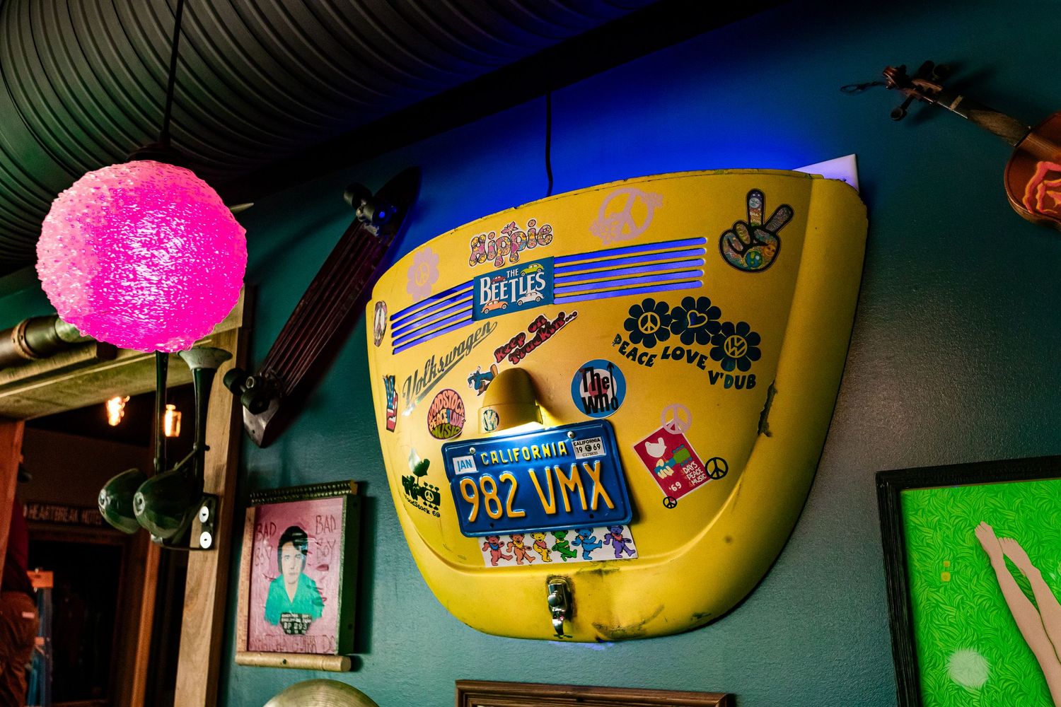 Yellow surfboard with stickers and decorative pink orb light mounted on dark wall.
