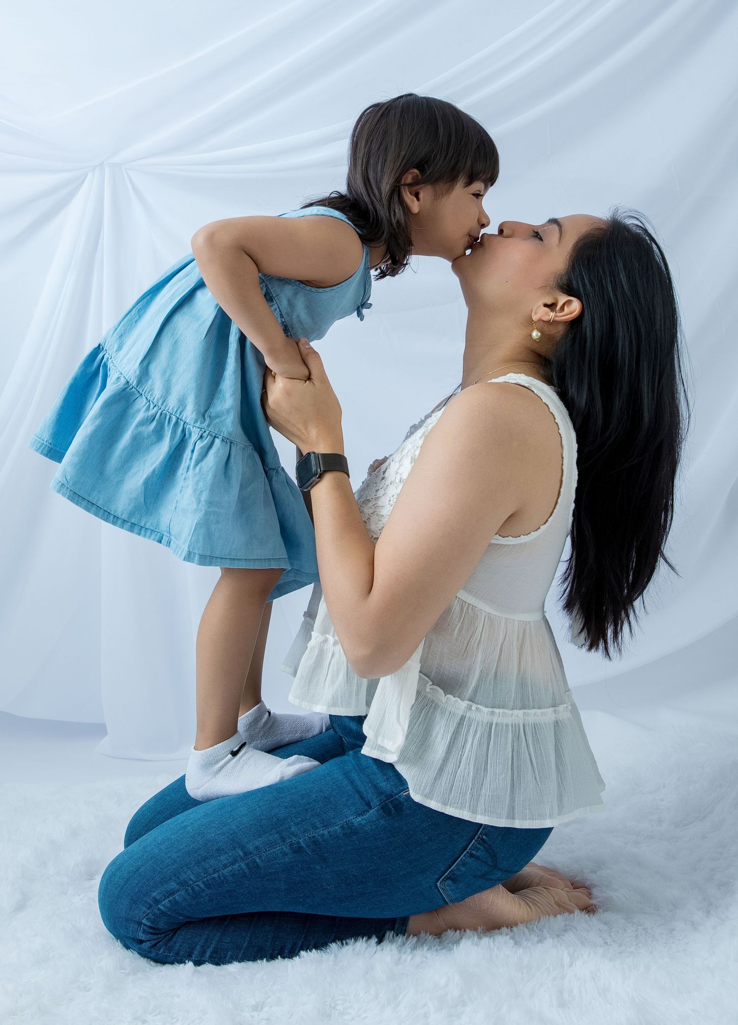 Sweet mother-child moment captured in white dresses against studio backdrop.