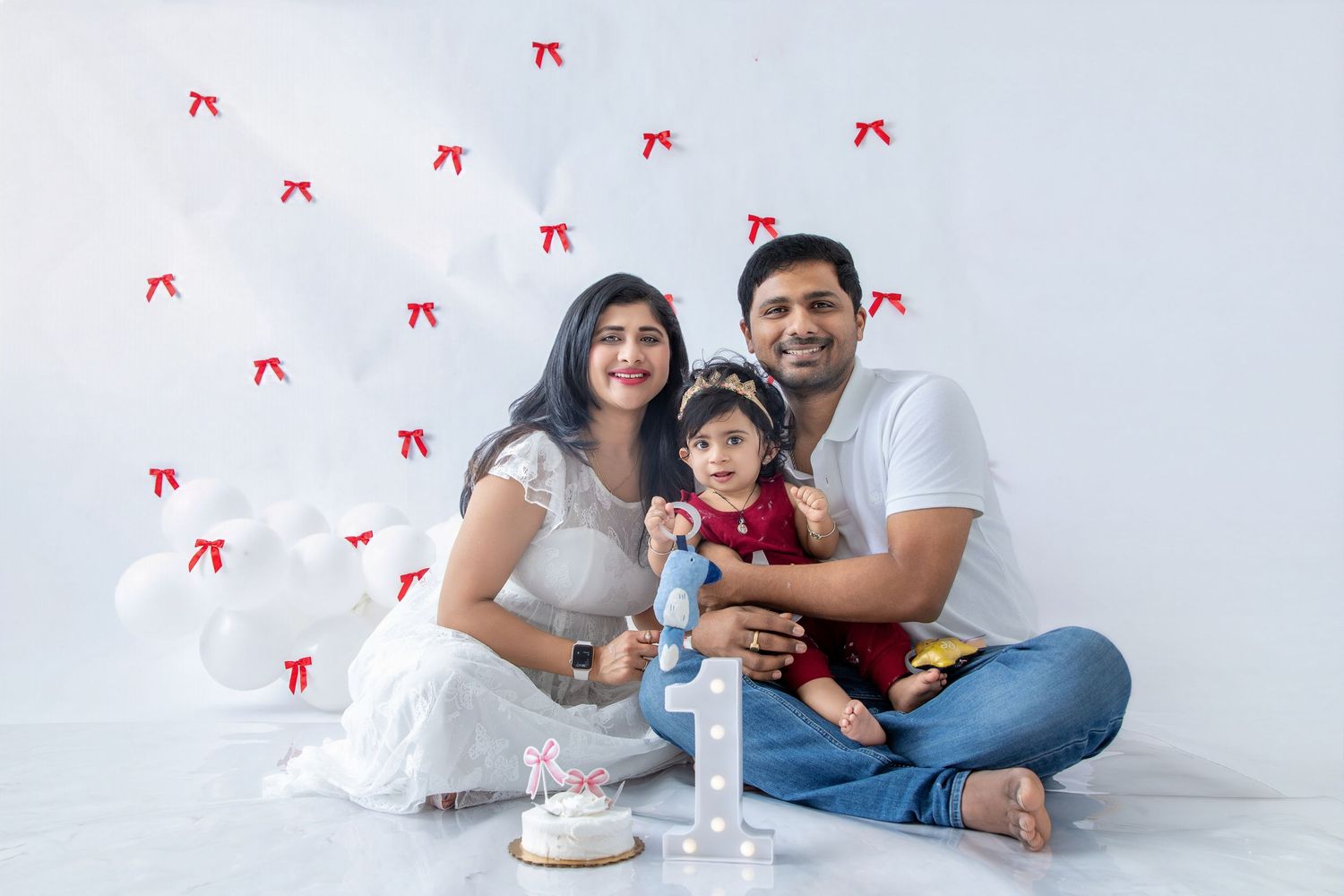 A relaxed family photo session with white balloons and red bows as backdrop elements.