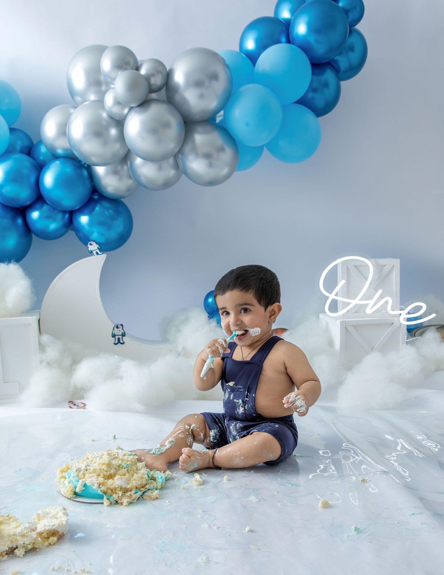 A messy cake smash scene with blue and silver balloon decor and scattered cake crumbs.
