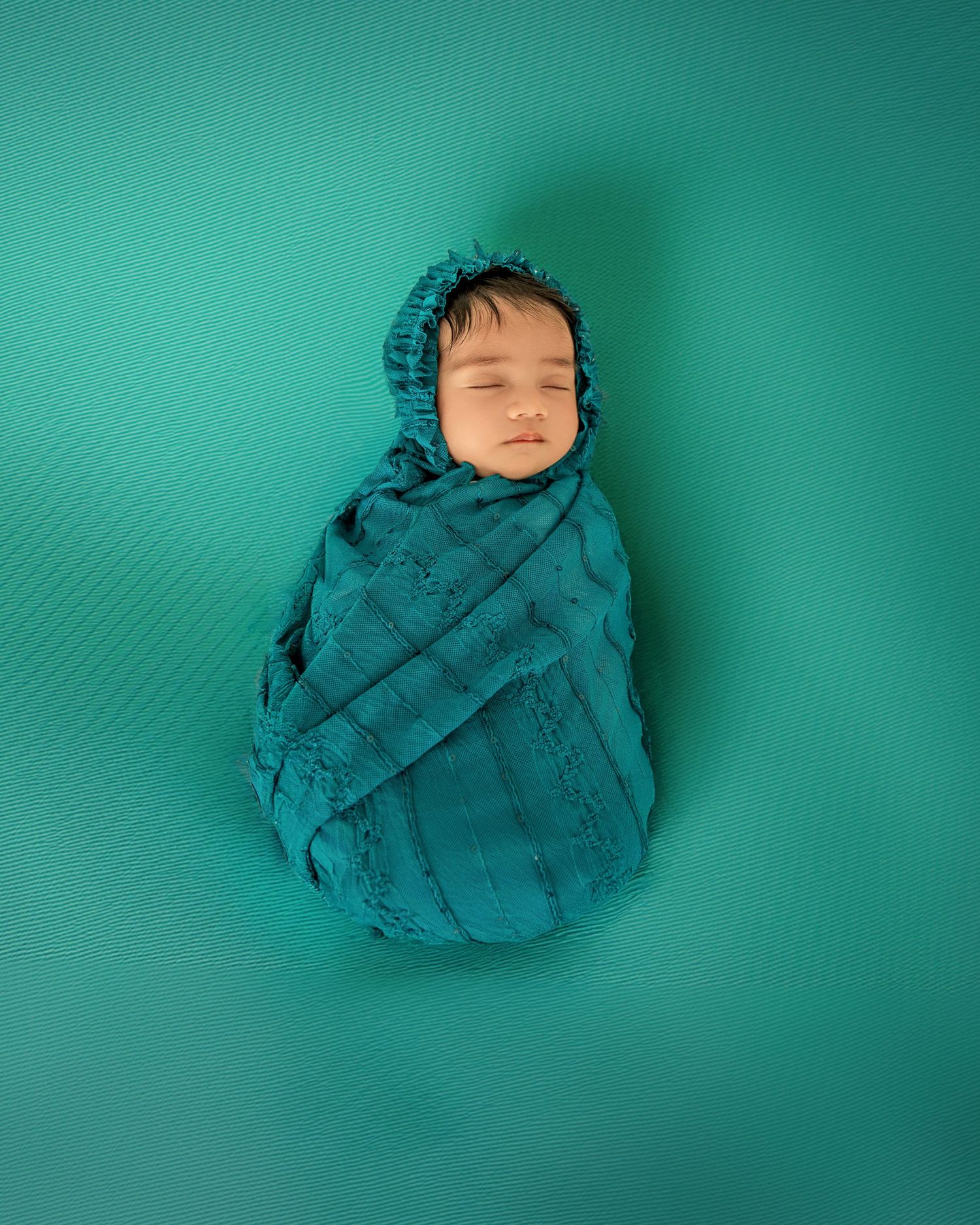 A sleeping newborn swaddled in a teal blanket lies on a turquoise background in a series of peaceful poses.