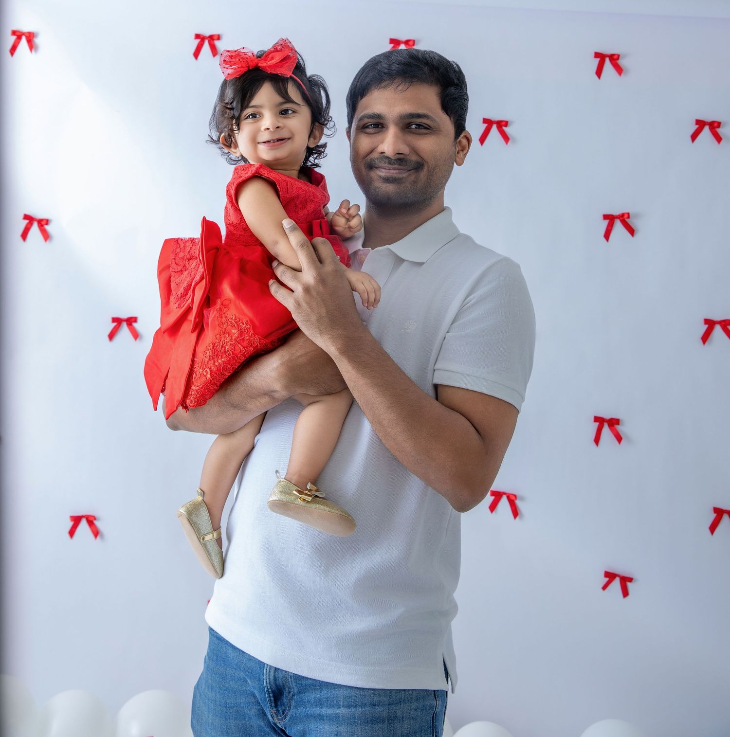Parent and toddler in red dress pose against backdrop with red bows.