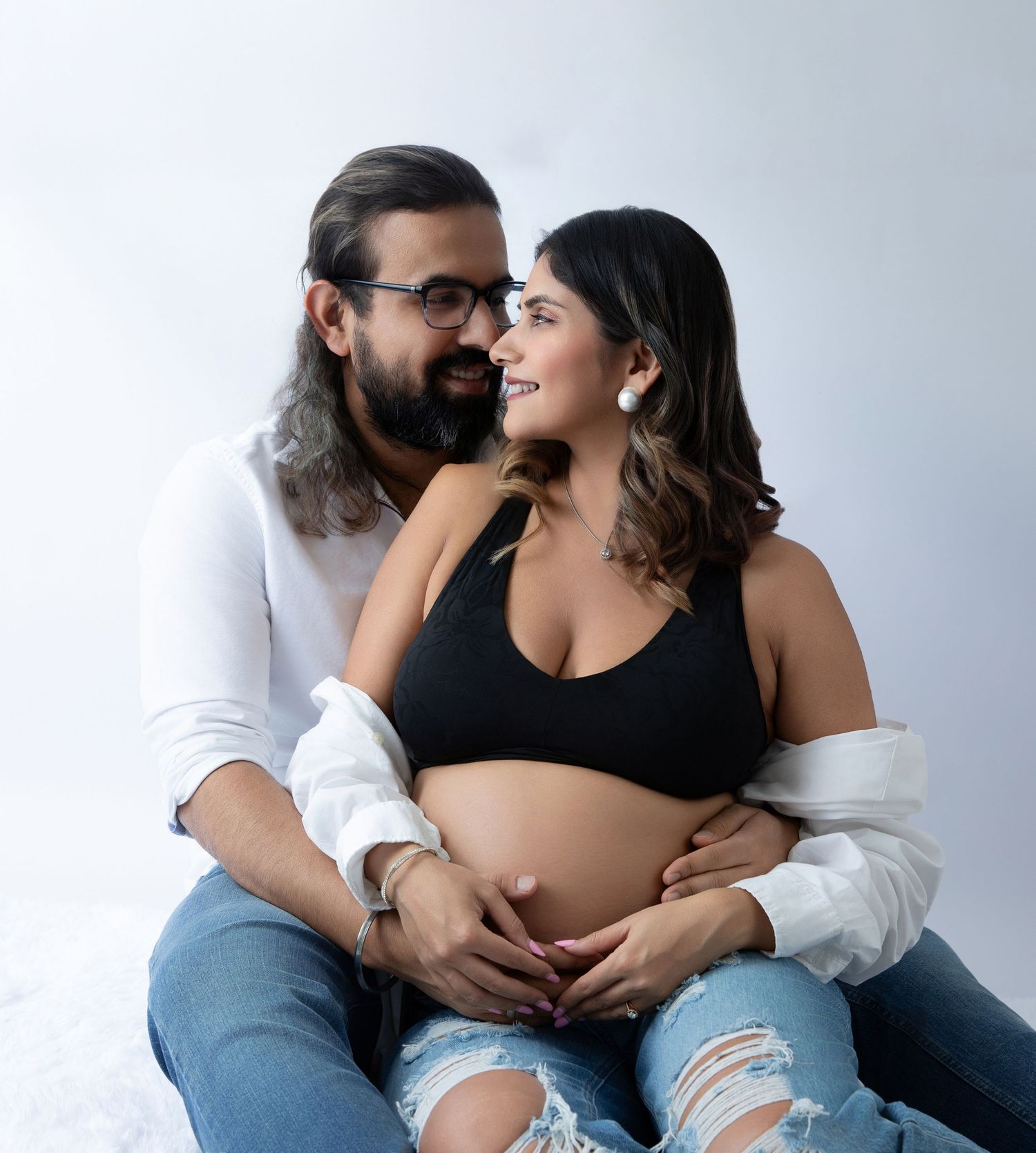 A couple sharing a tender moment during a maternity photoshoot, with the man embracing the pregnant woman from behind.